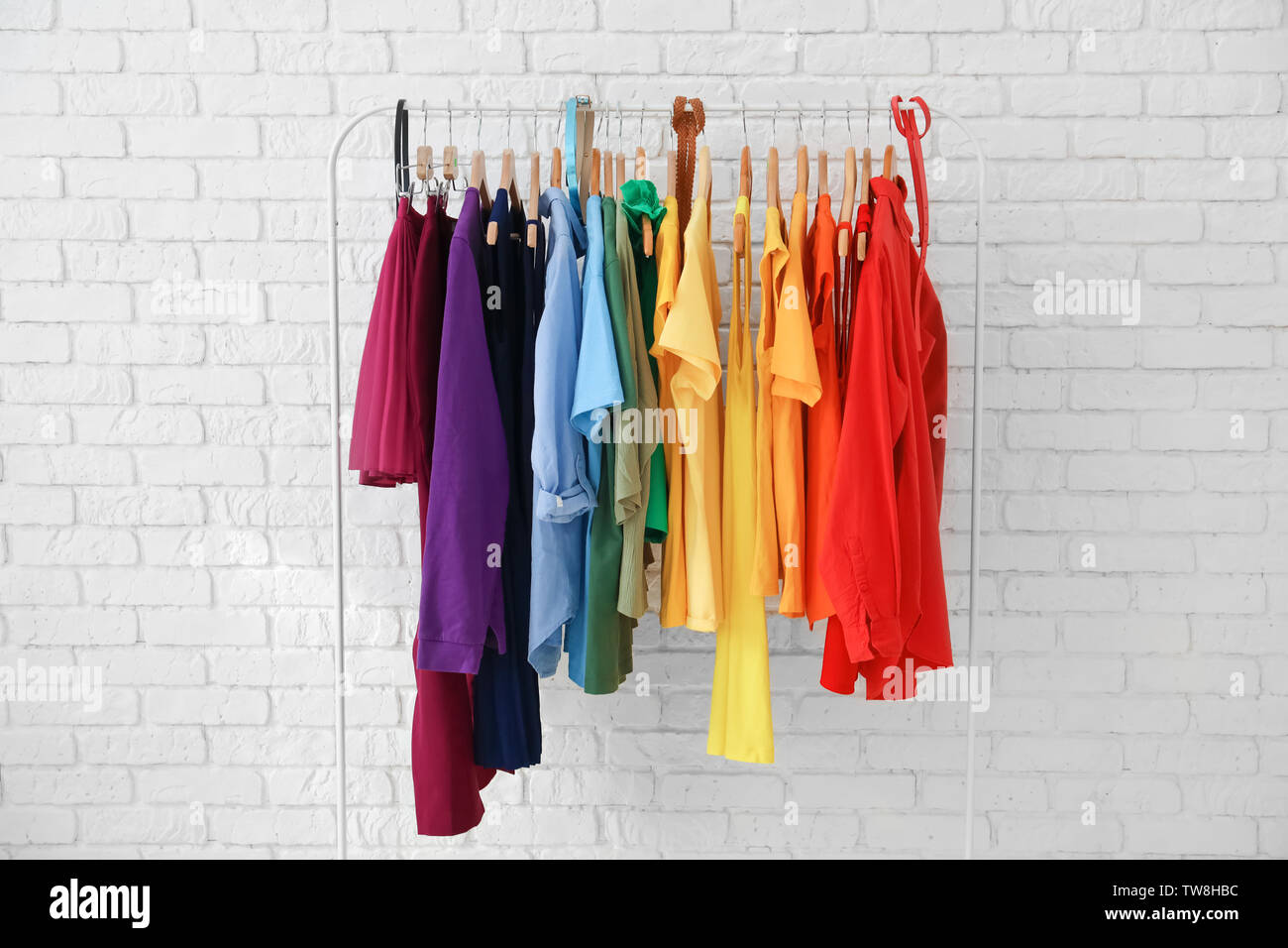 Rack with rainbow clothes near brick wall Stock Photo - Alamy
