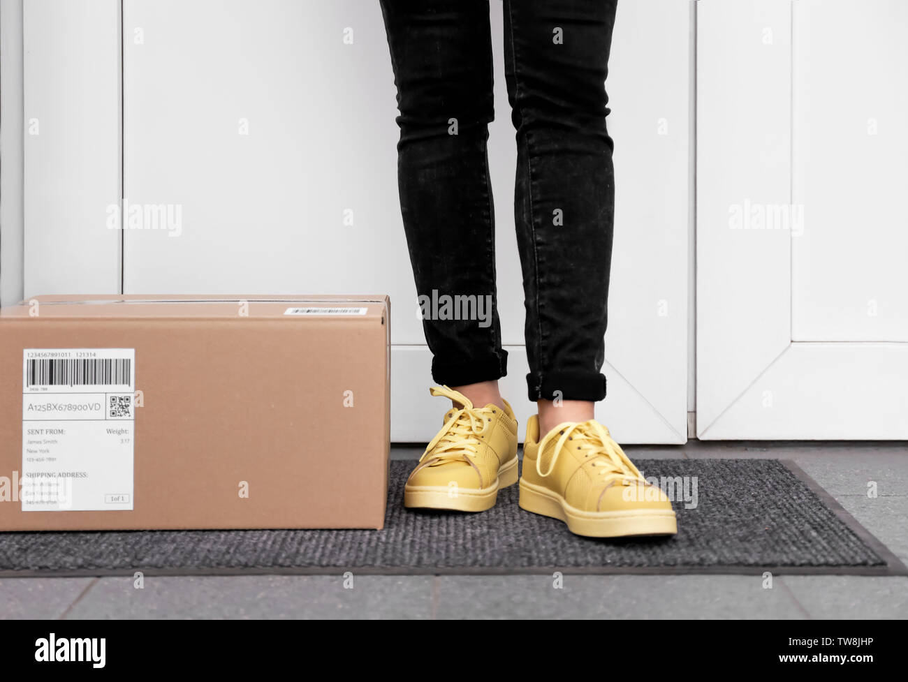 Woman standing near delivered parcel on doormat, closeup Stock Photo
