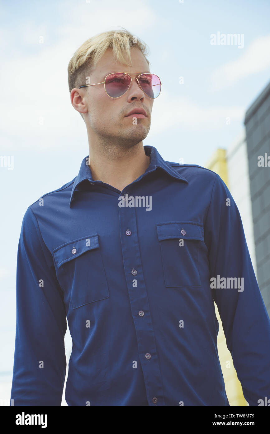 A Caucasian Blonde male model posing in a vintage 70s blue shirt, posing outdoor against a blue sky background. A vintage fashion editorial. Stock Photo