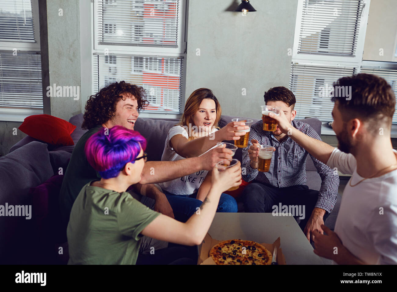 A group of friends is clinking glasses with beer in the room Stock Photo
