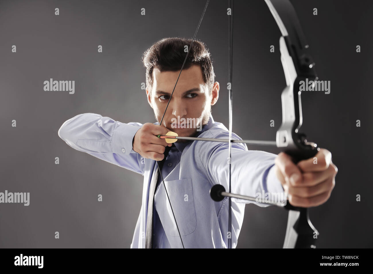 Young businessman practicing archery on dark background Stock Photo