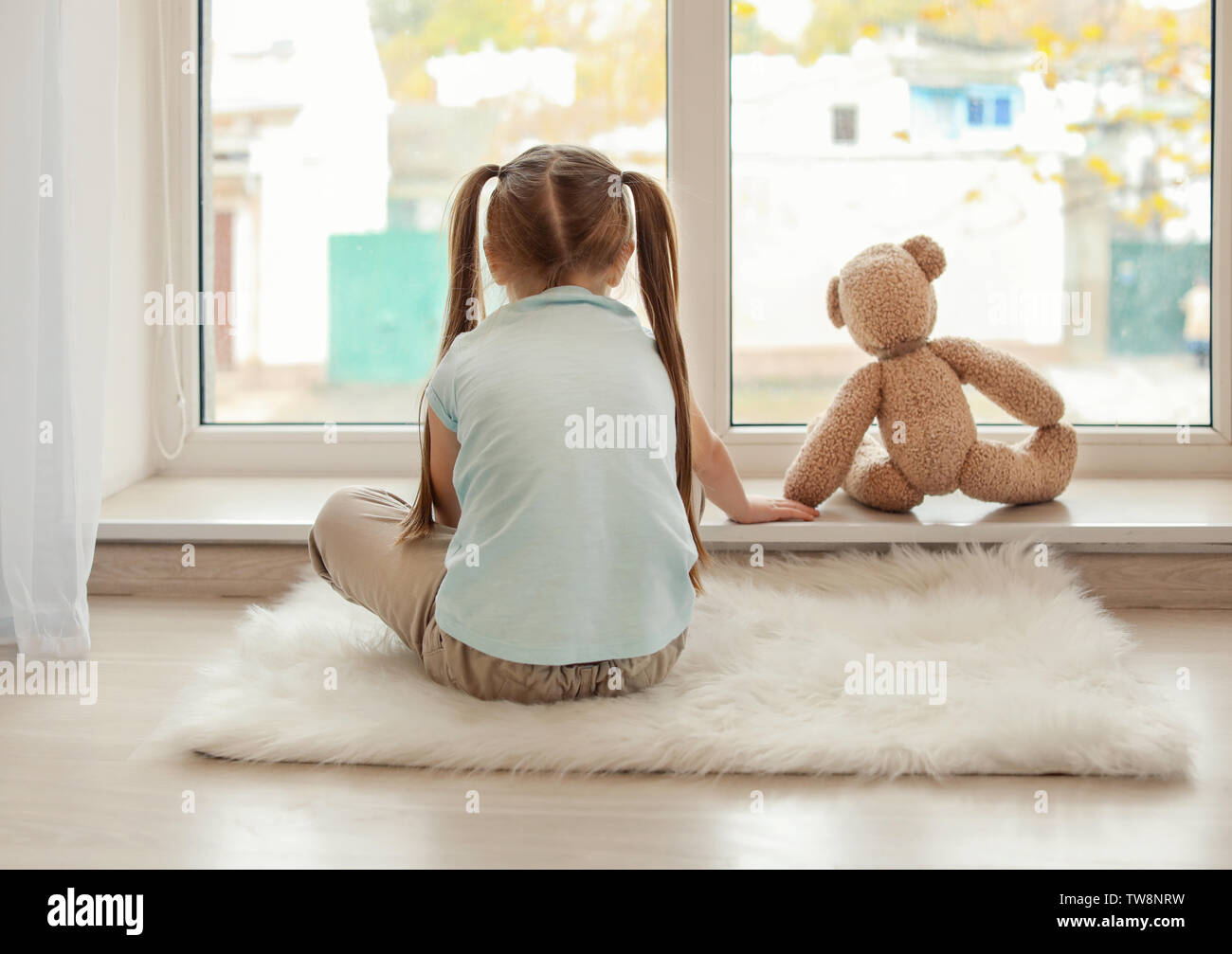 Lonely little girl with teddy bear sitting near window. Autism concept ...