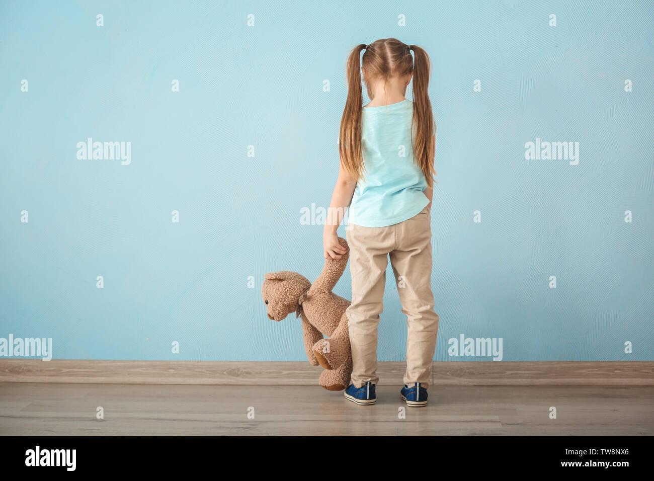 Lonely little girl with teddy bear near color wall. Autism concept ...