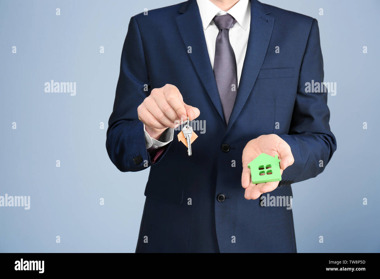 Real estate agent holding house model and key on grey background Stock ...