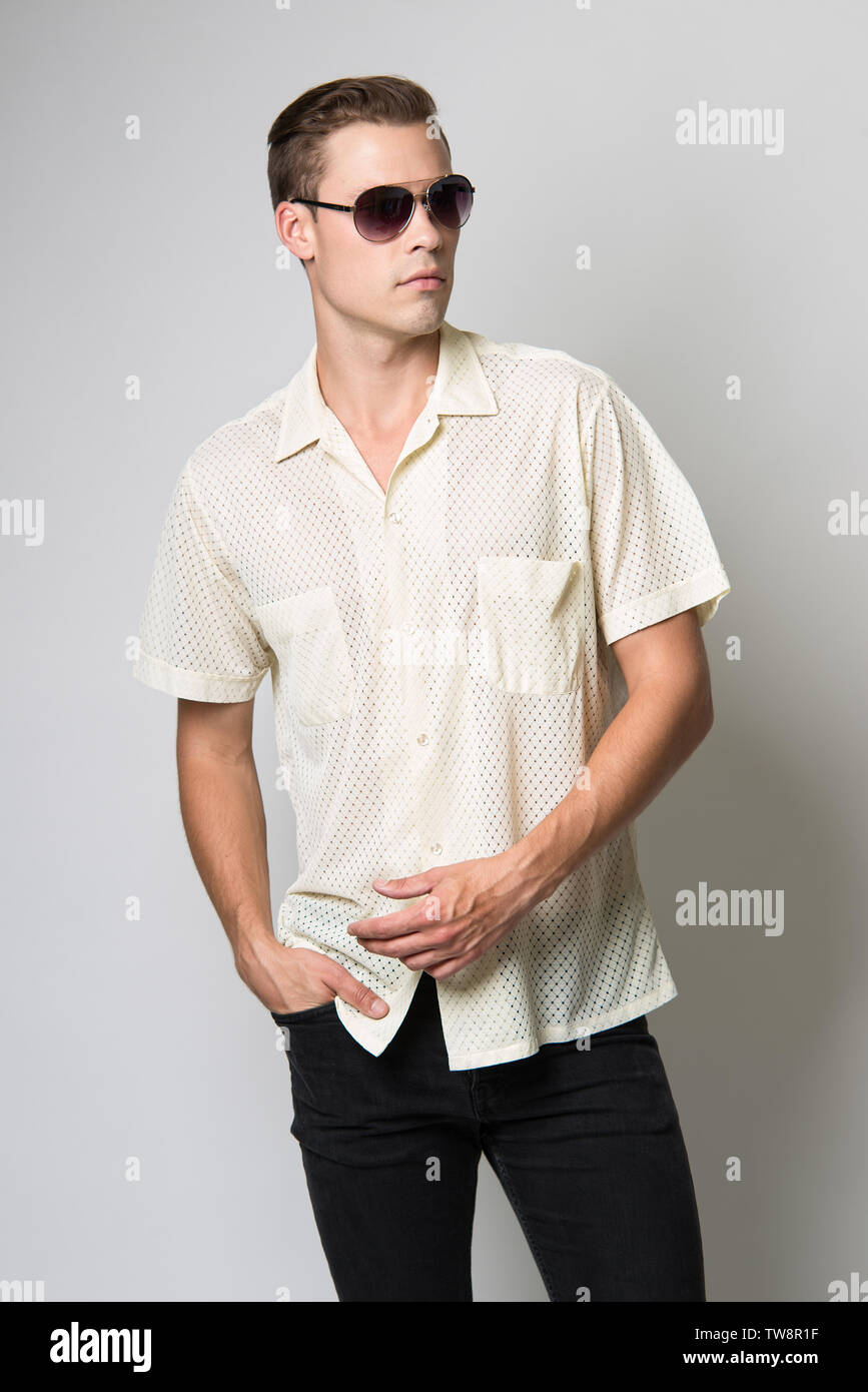 A White brown hair Caucasian male model posing in aviator sunglasses wearing a vintage light yellow 70s shirt. Stock Photo