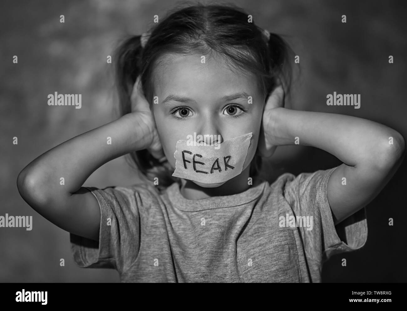 Sad little girl with taped mouth and word 'Fear' on grey background, black and white effect Stock Photo