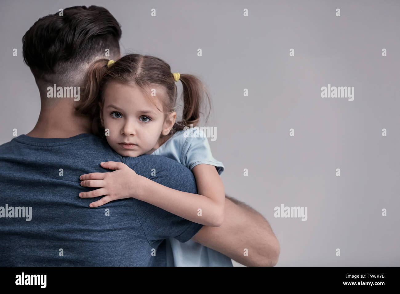 Sad little girl hugging her father on grey background Stock Photo