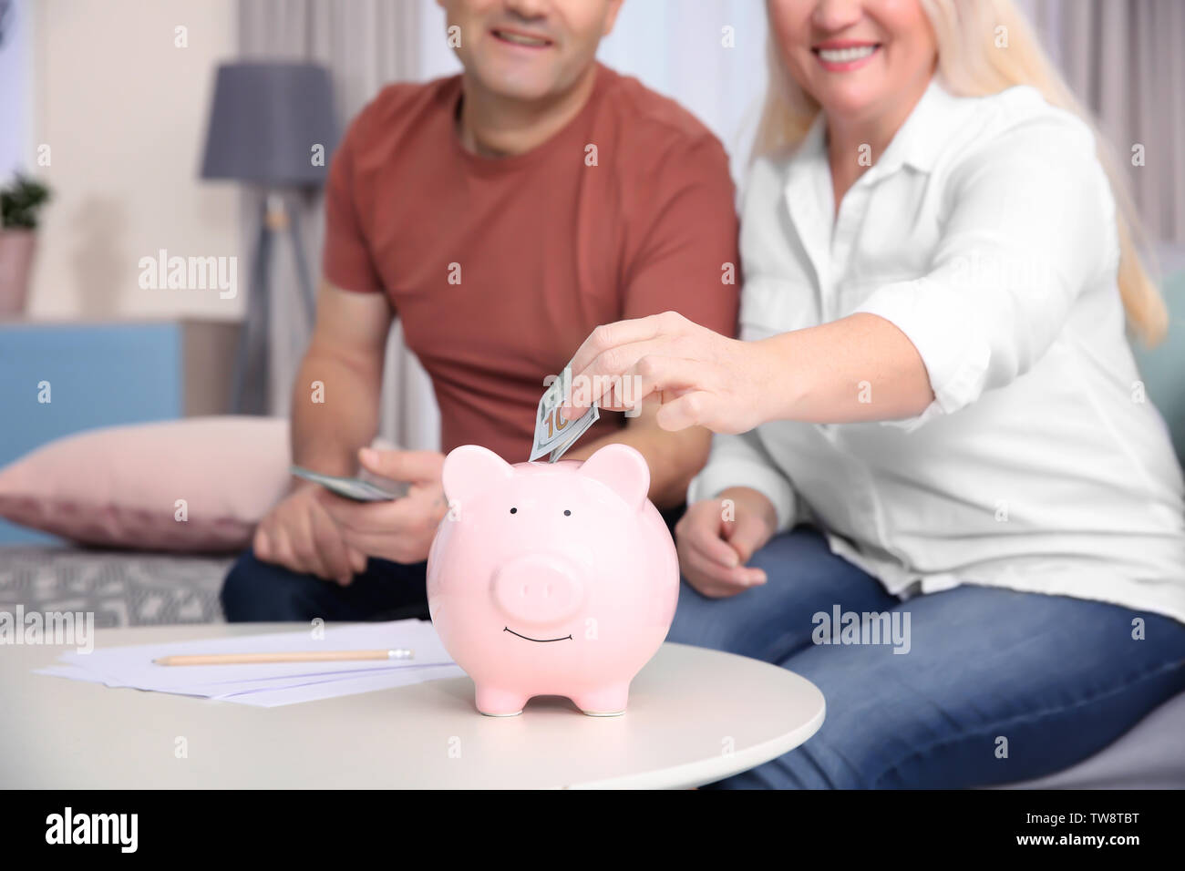 Mature couple putting money into piggy bank at home Stock Photo - Alamy