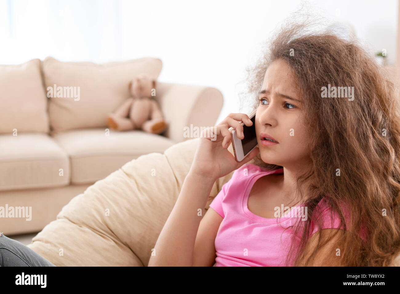 Depressed teenager talking on mobile phone in lounge chair Stock Photo
