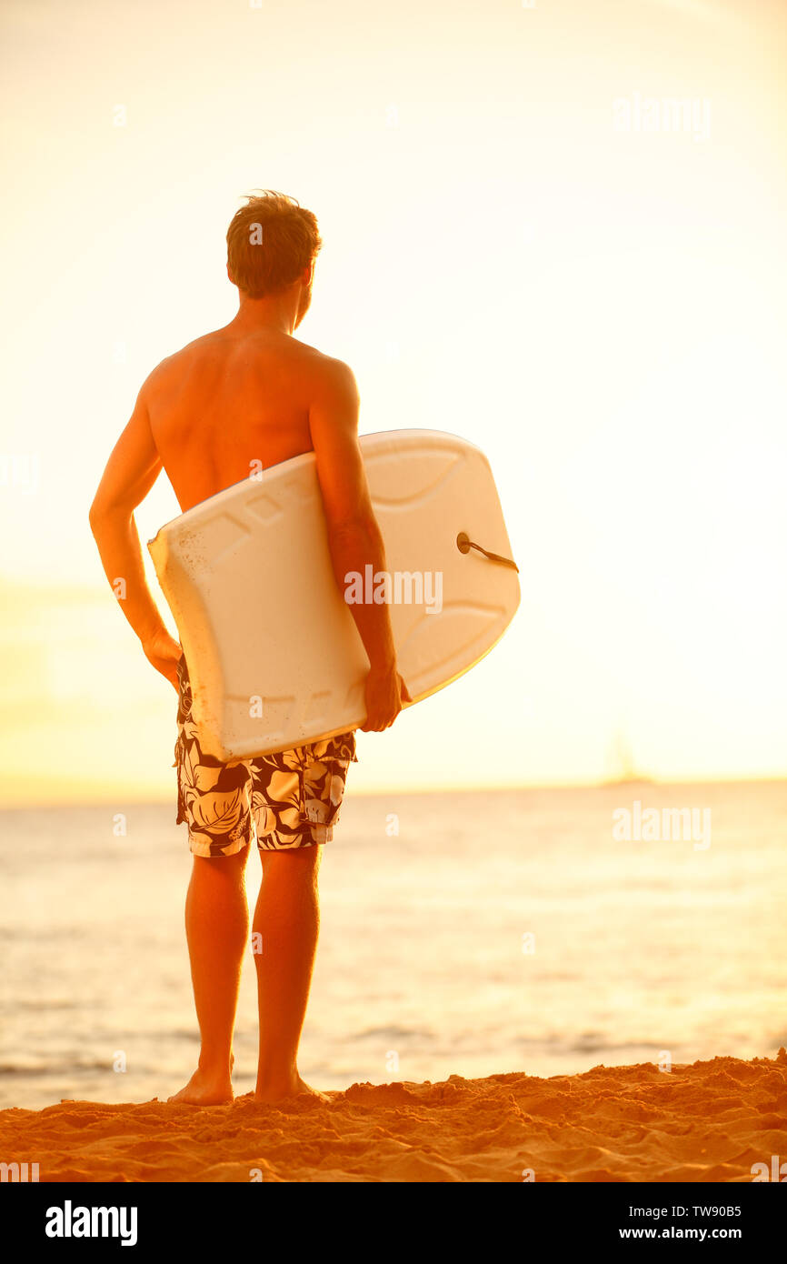 Surfer man on beach at surfing sunset holding bodyboard. Fit male body surfer guy enjoying sunset and bodyboarding on summer holidays vacation on tropical beach. Kaanapali beach, Maui, Hawaii. Stock Photo
