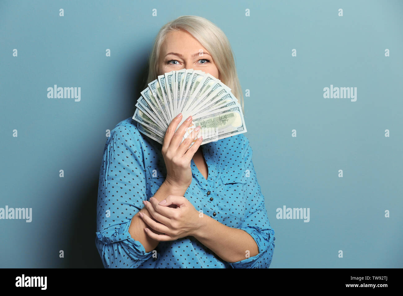 Happy mature woman with lot of dollar banknotes on color background ...
