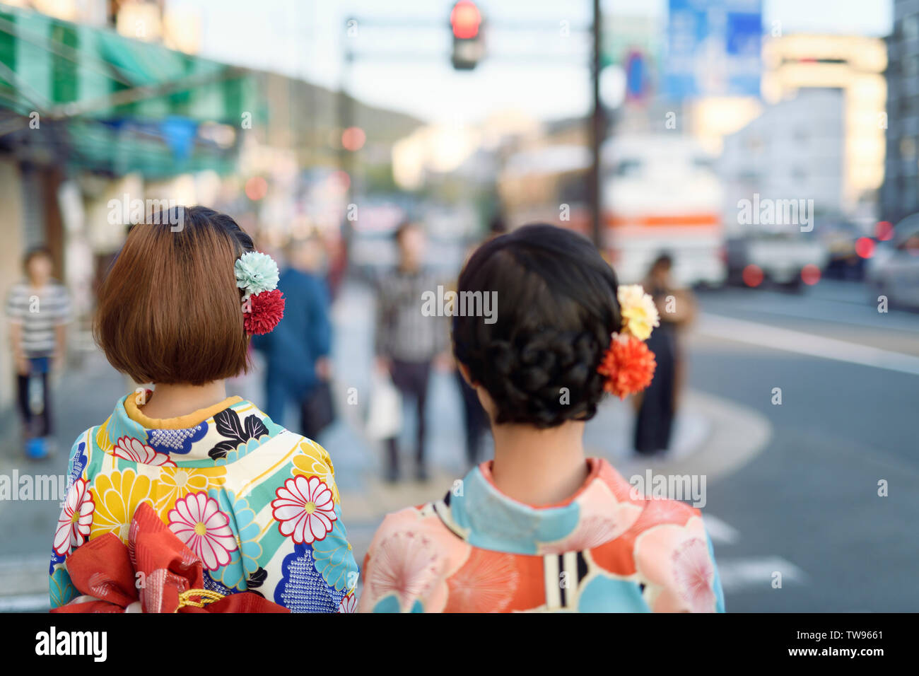 Two Japanese girls in bright Yukatas, and colorful flowers in their hair, walking on the streets of Kyoto, Japan. Stock Photo