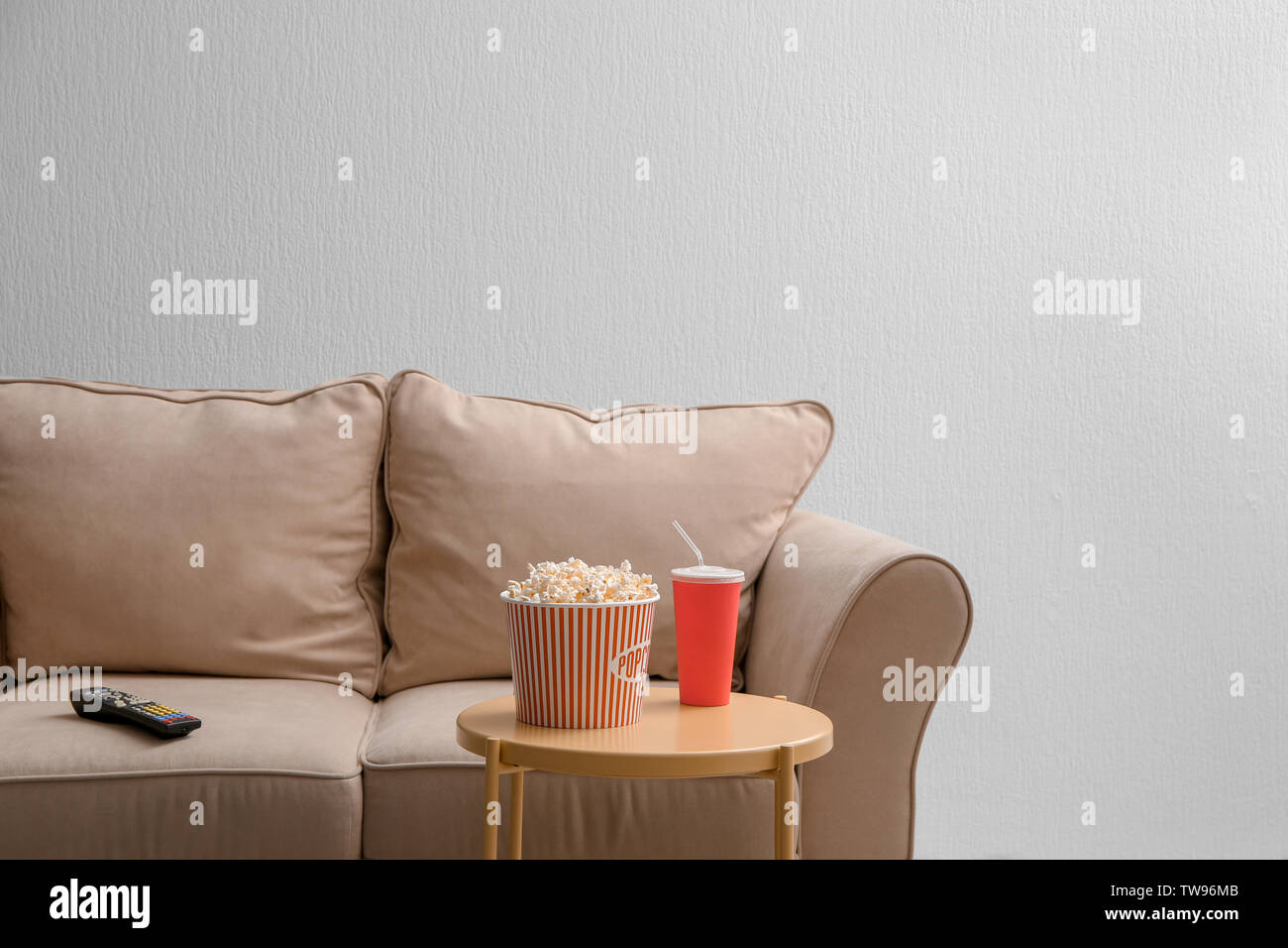 Comfortable couch with TV remote control and snack on table indoors. Home cinema Stock Photo