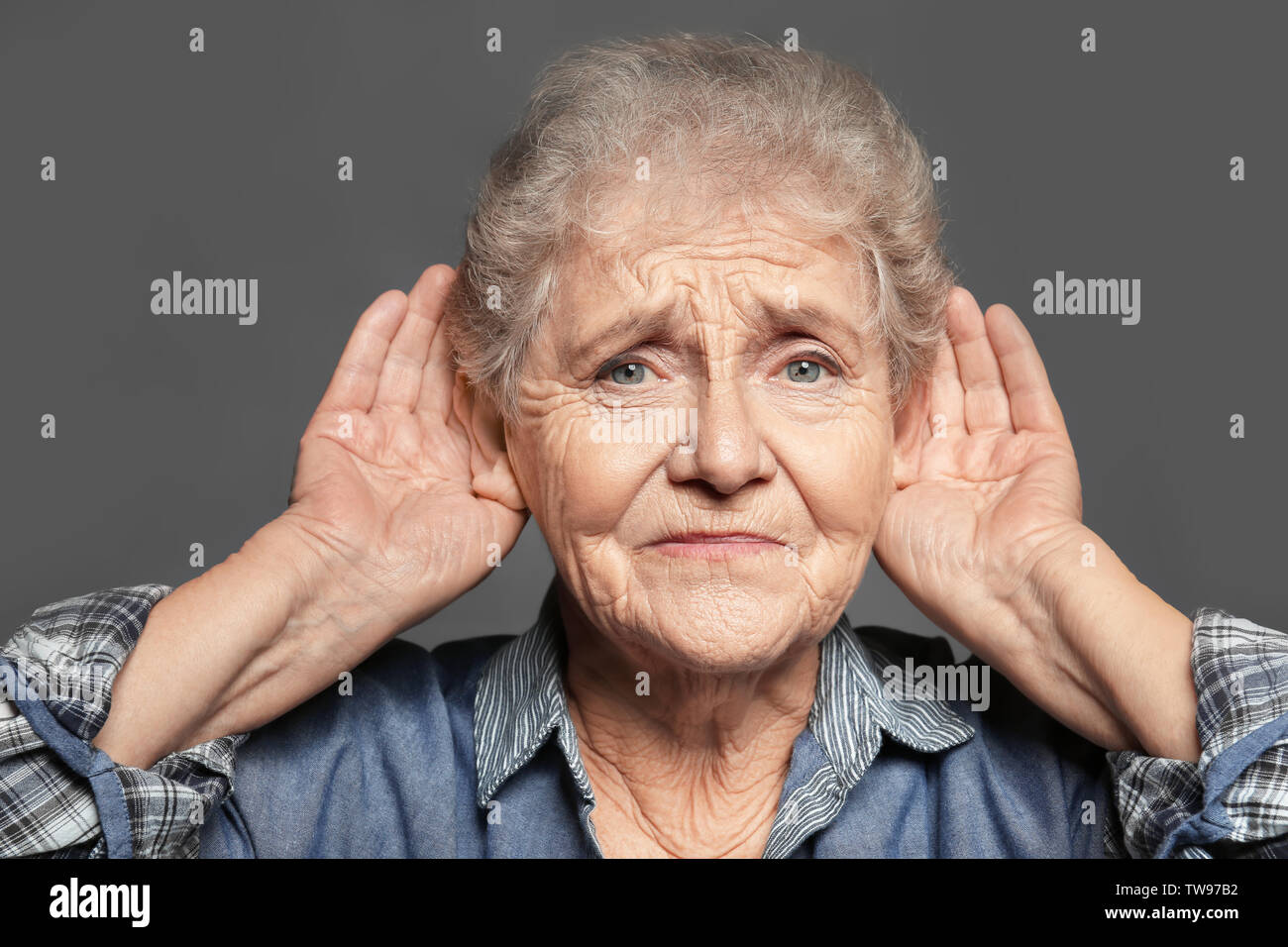 Elderly woman with hearing problem on grey background Stock Photo