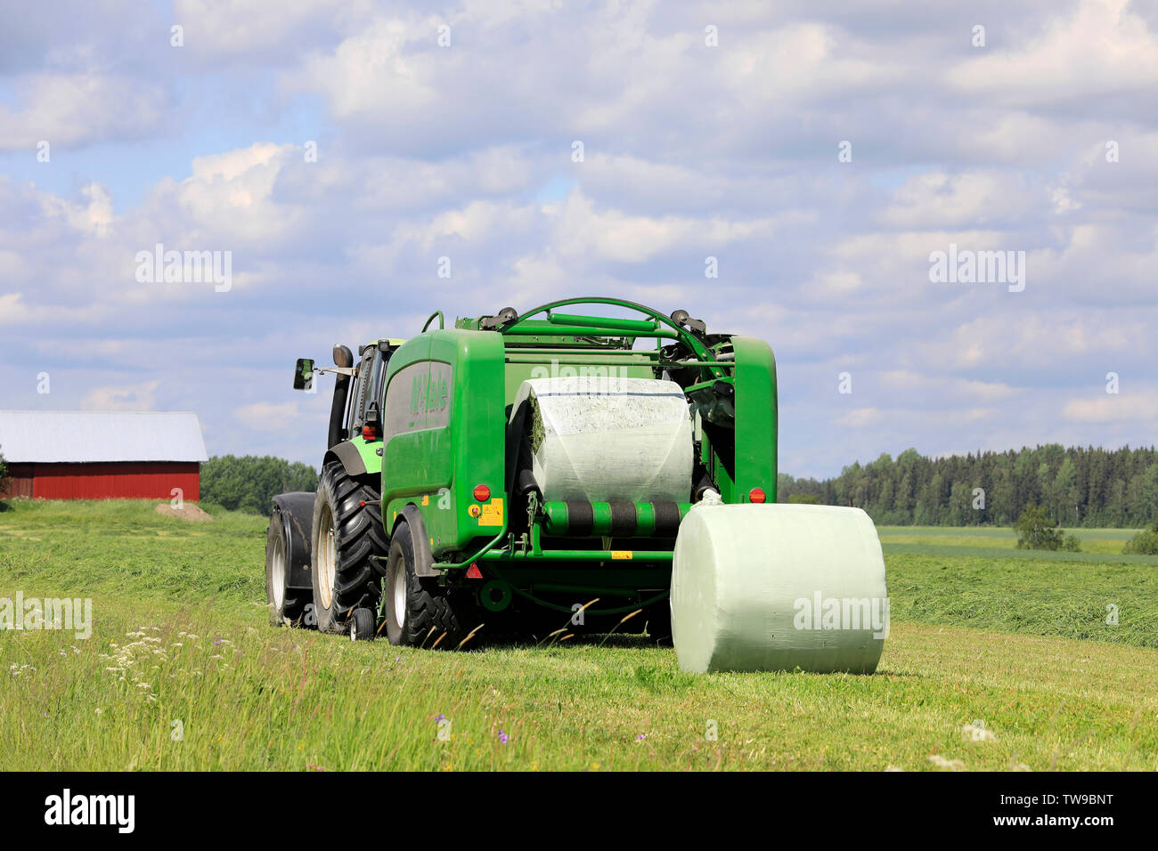 Salo, Finland. June 15, 2019. Deutz-Fahr tractor and McHale 3 plus baler baling silage in green plastic sheet in hay field on a sunny day of summer. Stock Photo