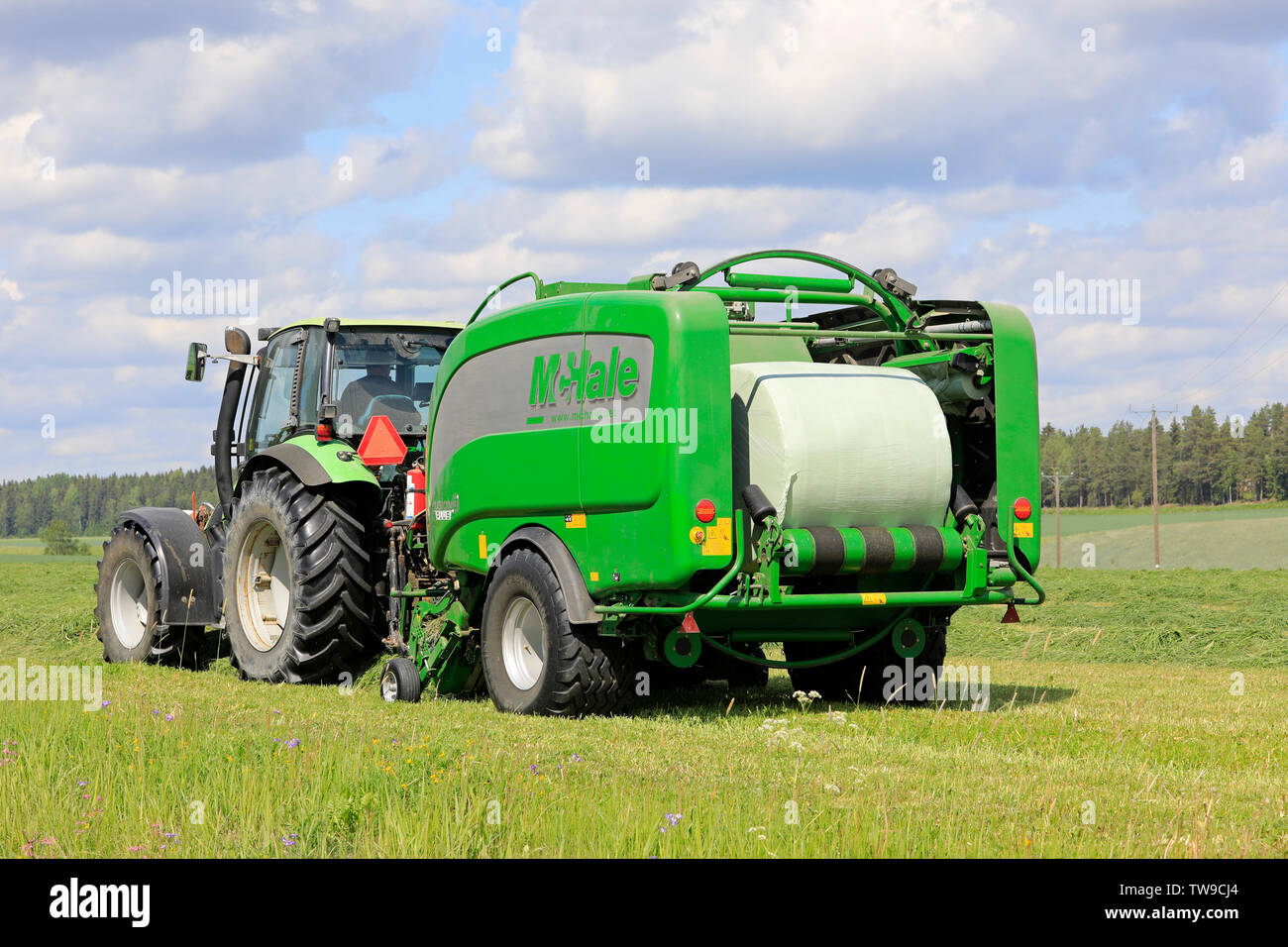 Salo, Finland. June 15, 2019. Deutz-Fahr tractor and McHale 3 plus baler baling silage in green plastic sheet in hay field on a sunny day of summer. Stock Photo