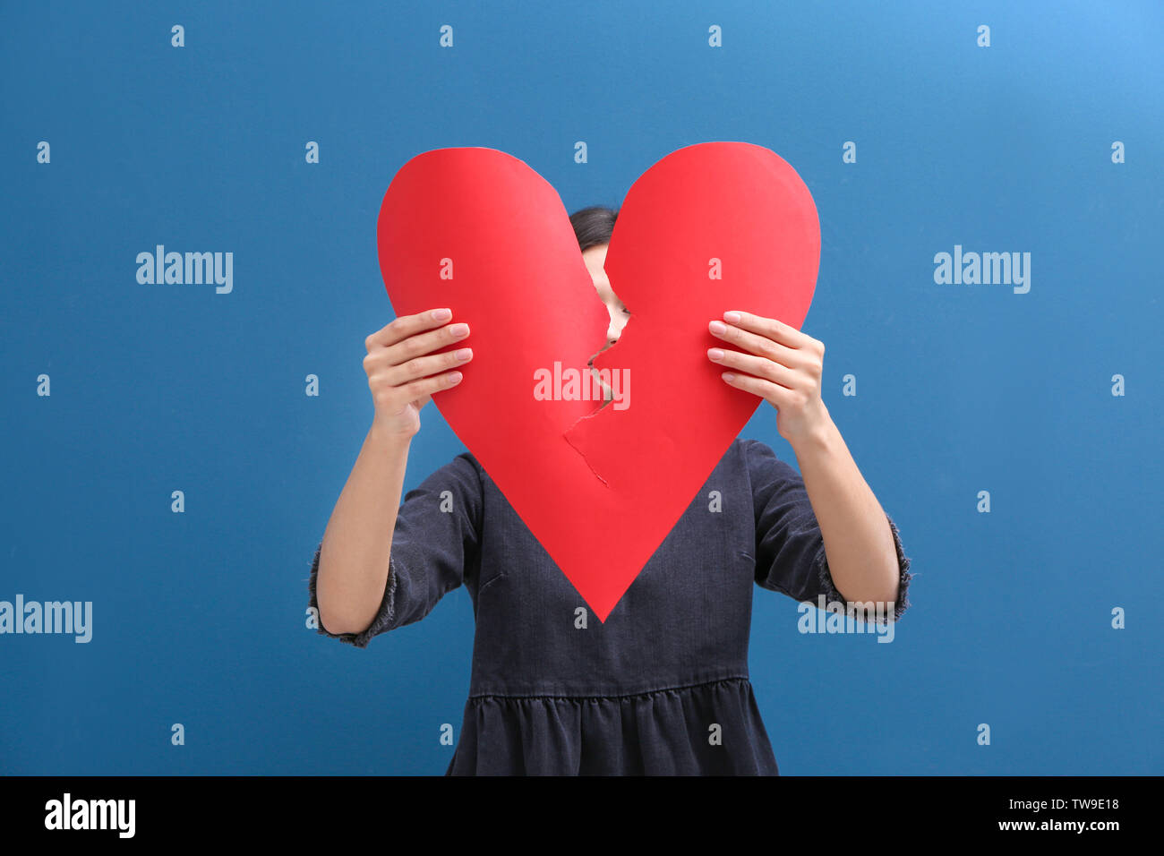 Young woman tearing paper heart in half on color background ...