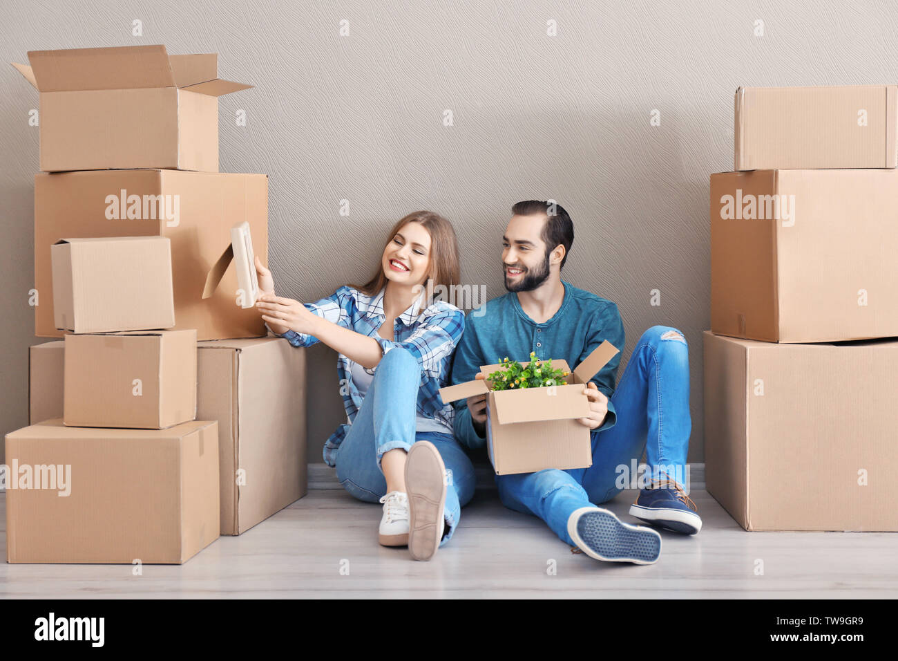 Young couple with moving boxes on floor in room Stock Photo