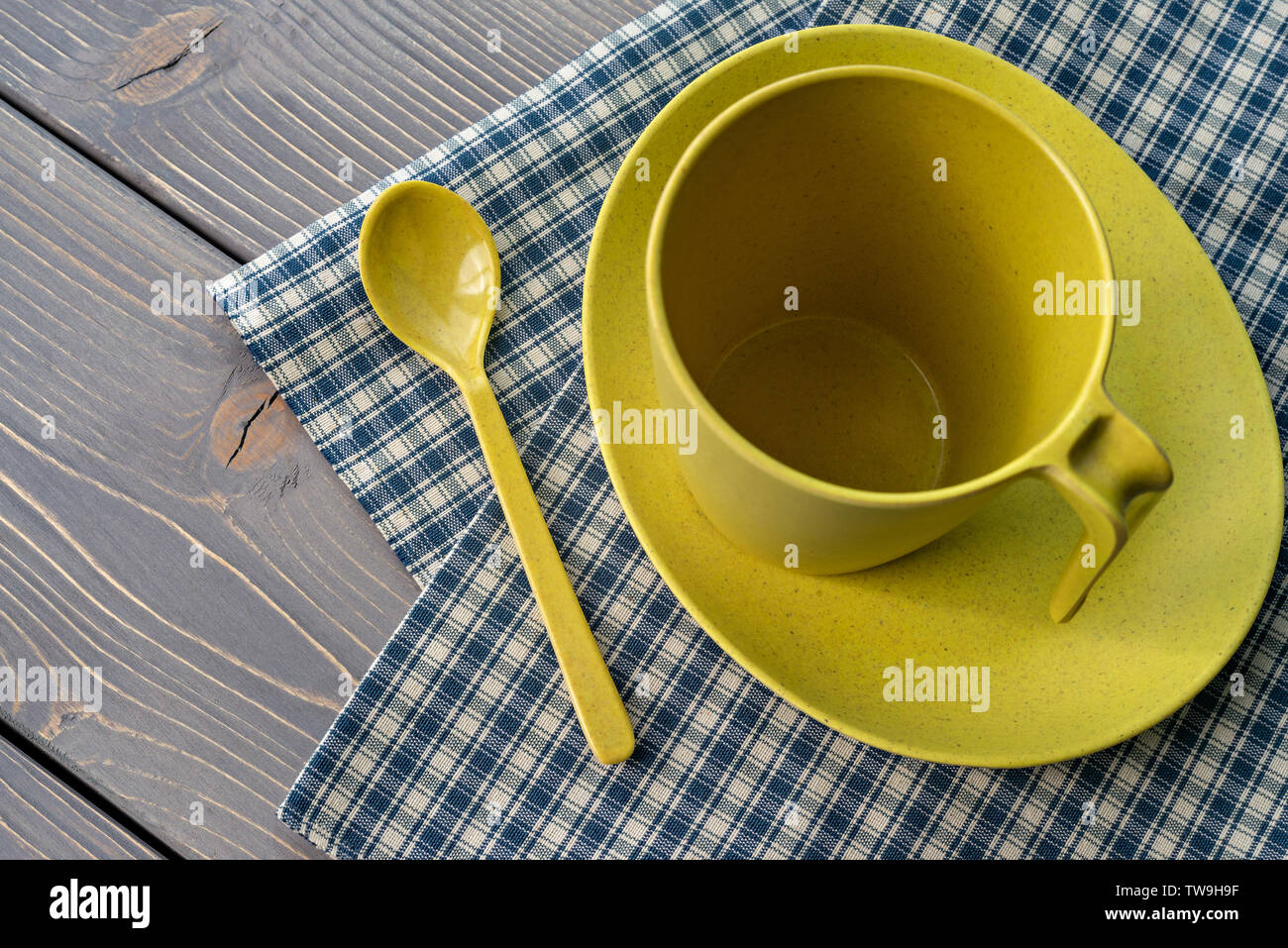 Yellow cup on a saucer with a spoon. Utensils of bamboo, with a checkered napkin on a wooden table. Shallow depth of field. Stock Photo