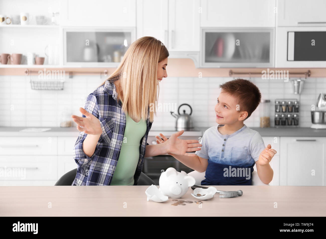 Mother and little son with broken piggy bank on table at home Stock Photo