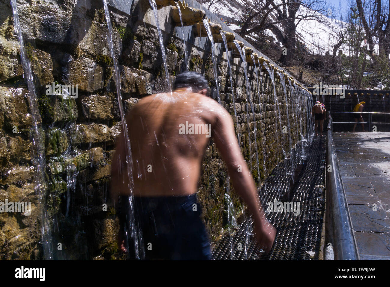 Muktinath Temple, sacred to both Hindu and Buddhists, Nepal.  Picture shows people walking under water fountains at the temple as a religious rite Stock Photo