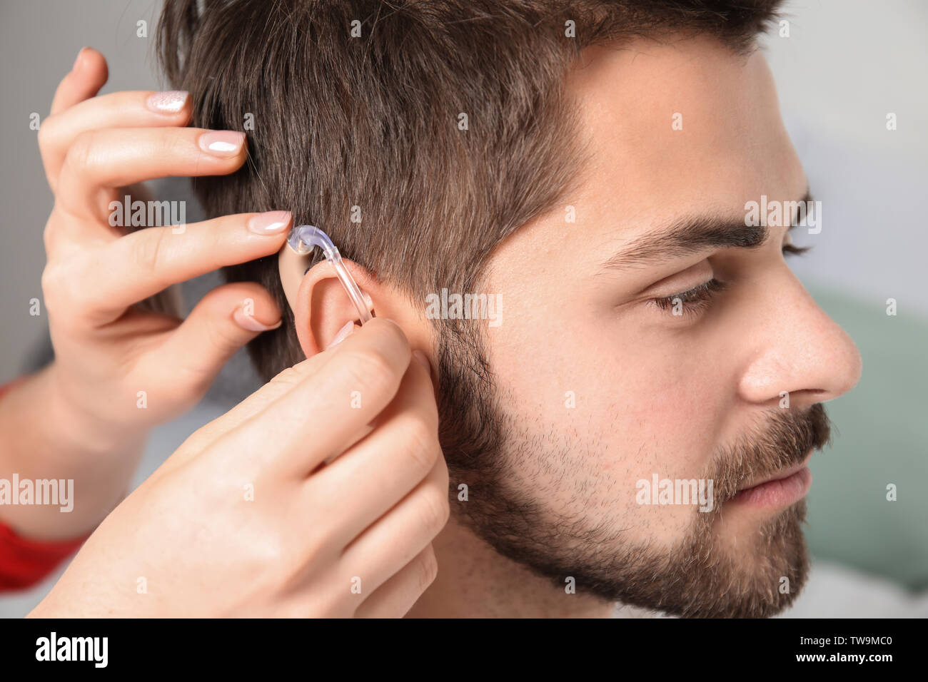 Doctor putting hearing aid in man's ear indoors Stock Photo - Alamy