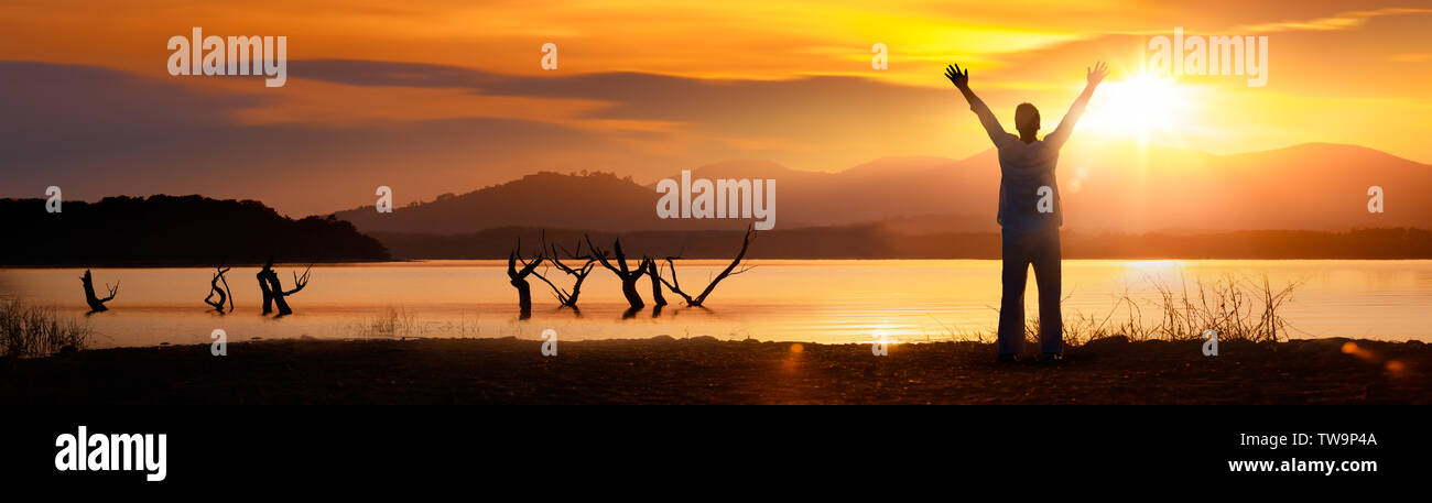 Silhouette of a man from the back with his hands up against the sunset Stock Photo