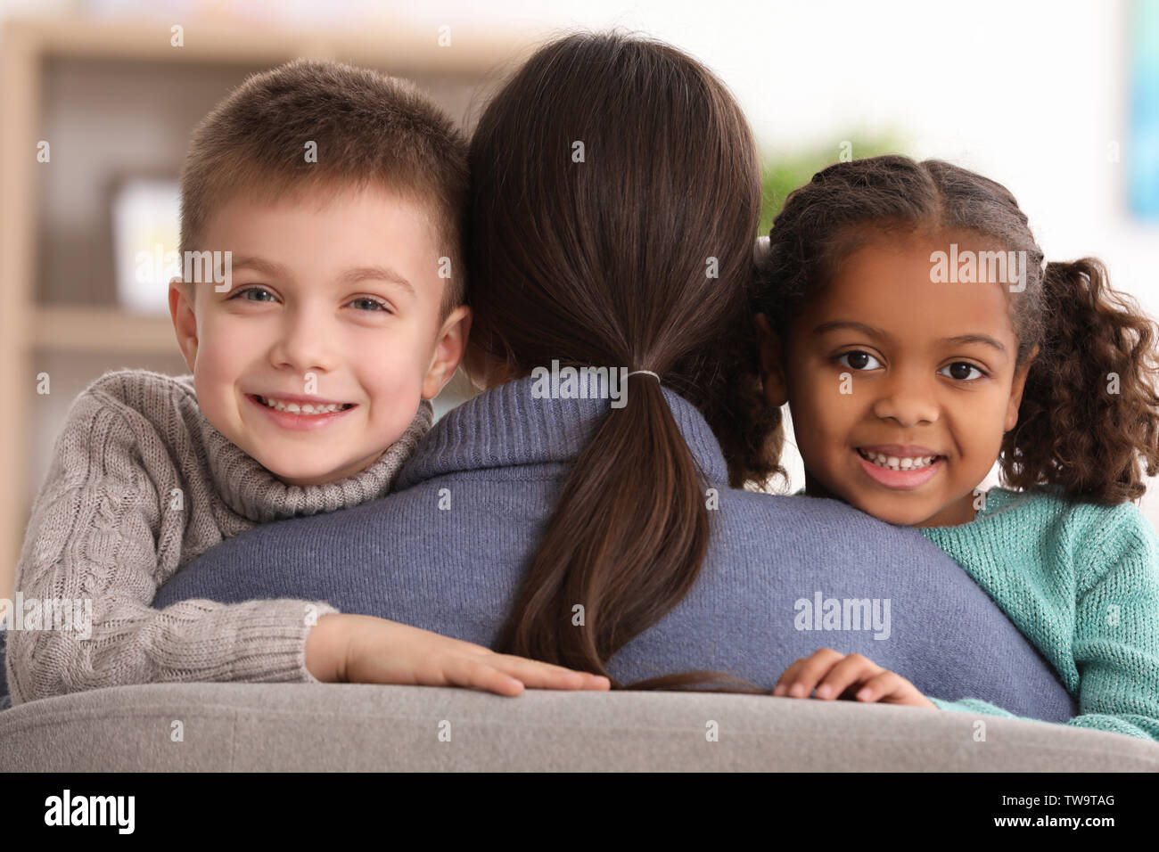 Woman hugging little kids indoors. Child adoption Stock Photo