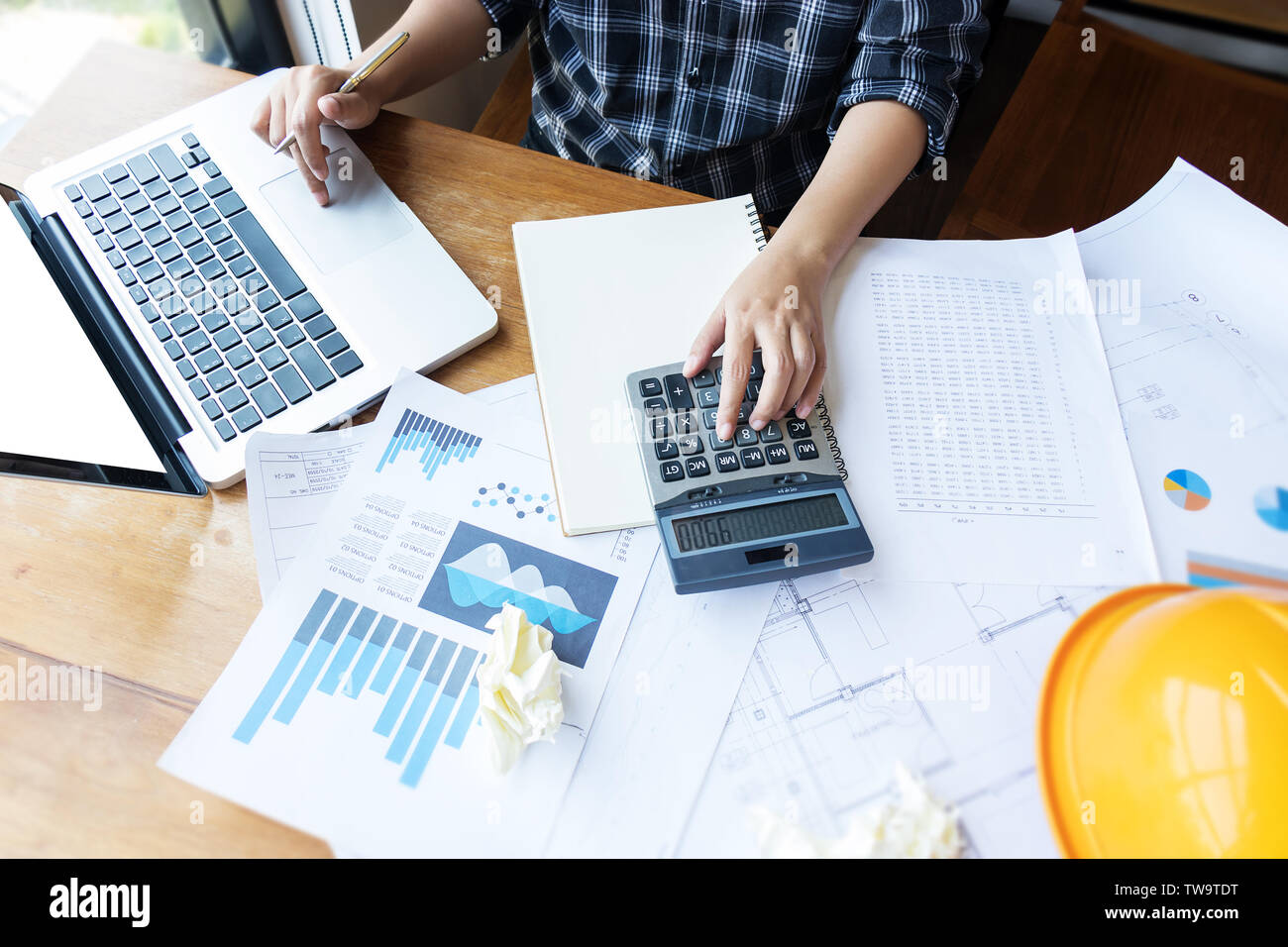 Asian engineer , architect woman using calculator for accounting and analyzing building structure from blueprint and paper chart in front of computer Stock Photo