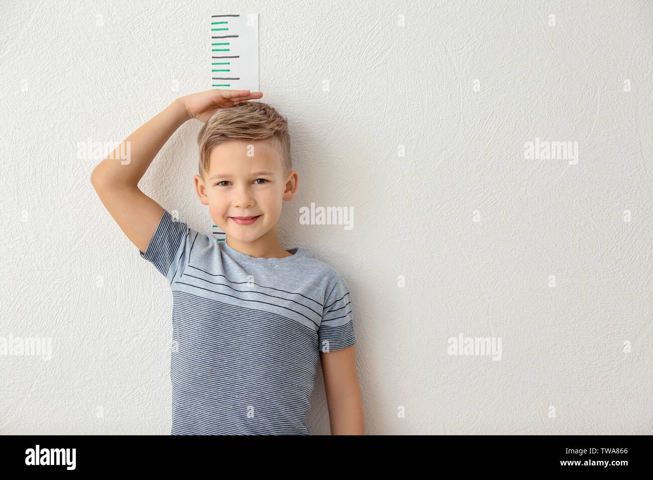 Cute little boy measuring height near light wall Stock Photo