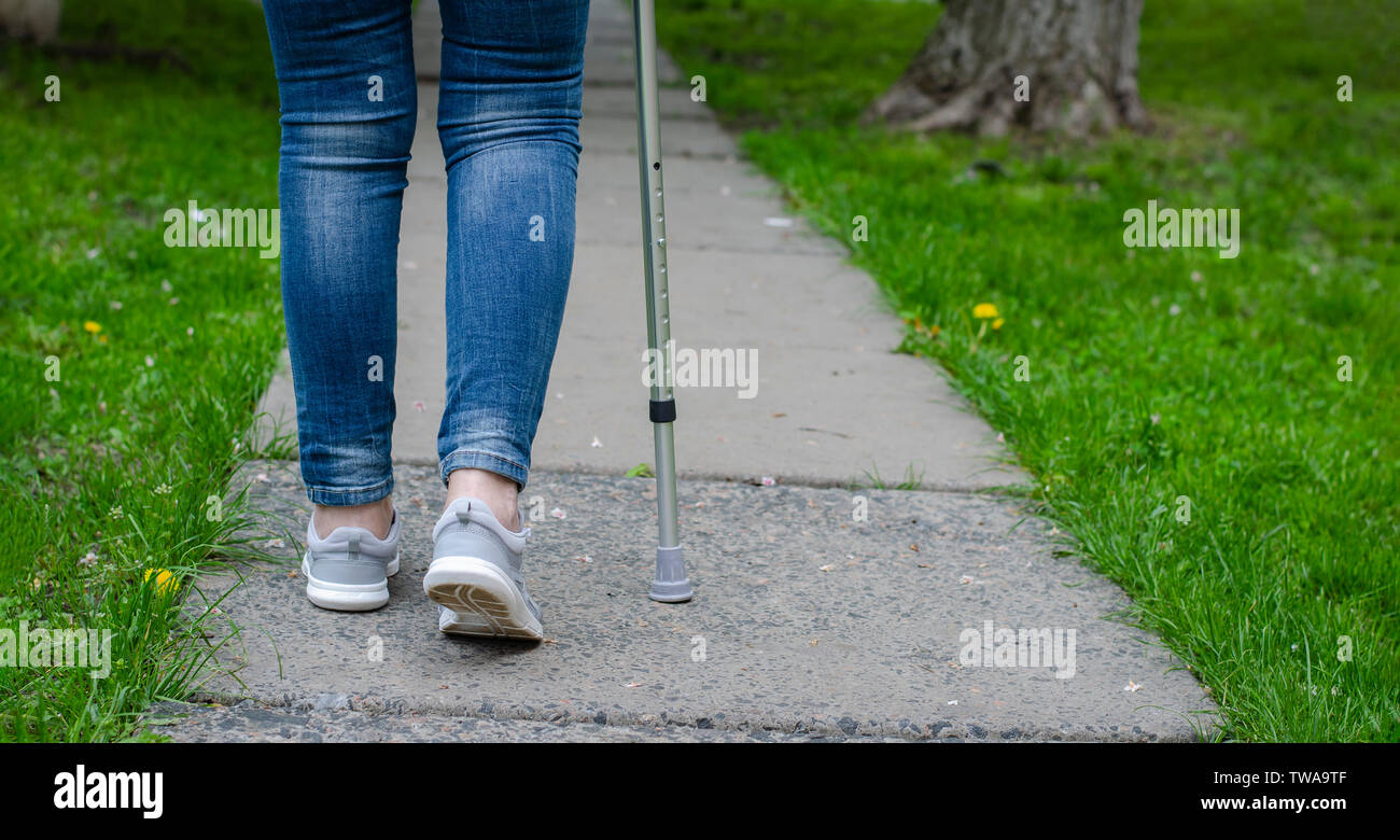 Senior woman in jeans walks with walking cane outdoors. Rehabilitation and recovery concept. Copy space Stock Photo