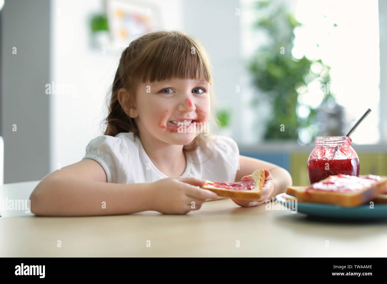 Cute little girl eating toast with jam at home Stock Photo - Alamy