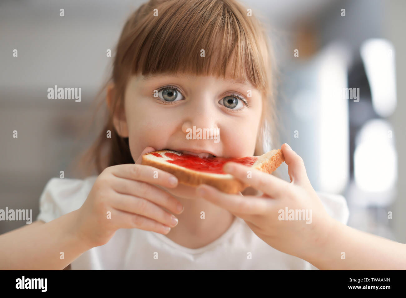 Cute little girl eating toast with jam at home Stock Photo - Alamy