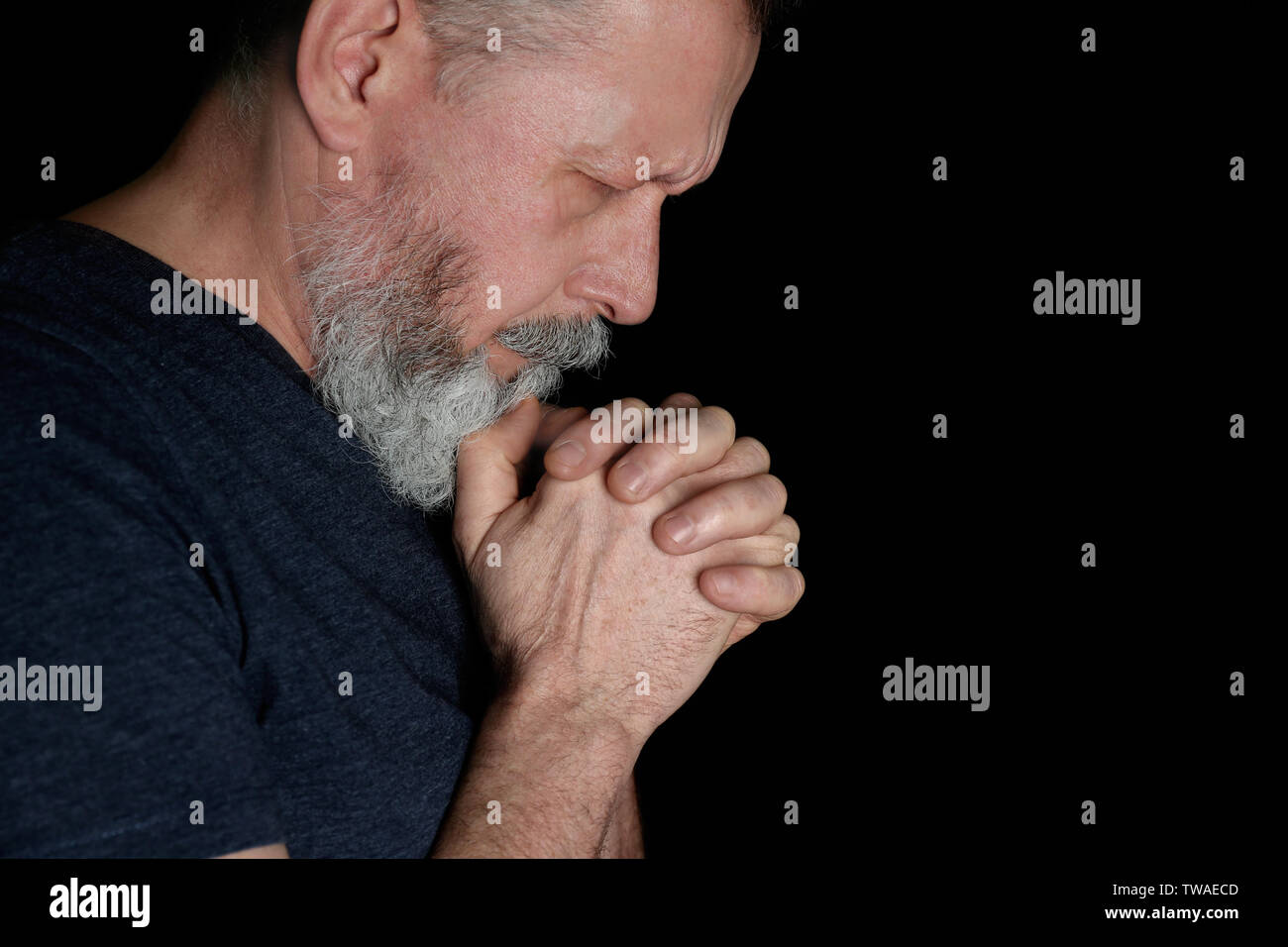 Religious senior man praying on black background Stock Photo