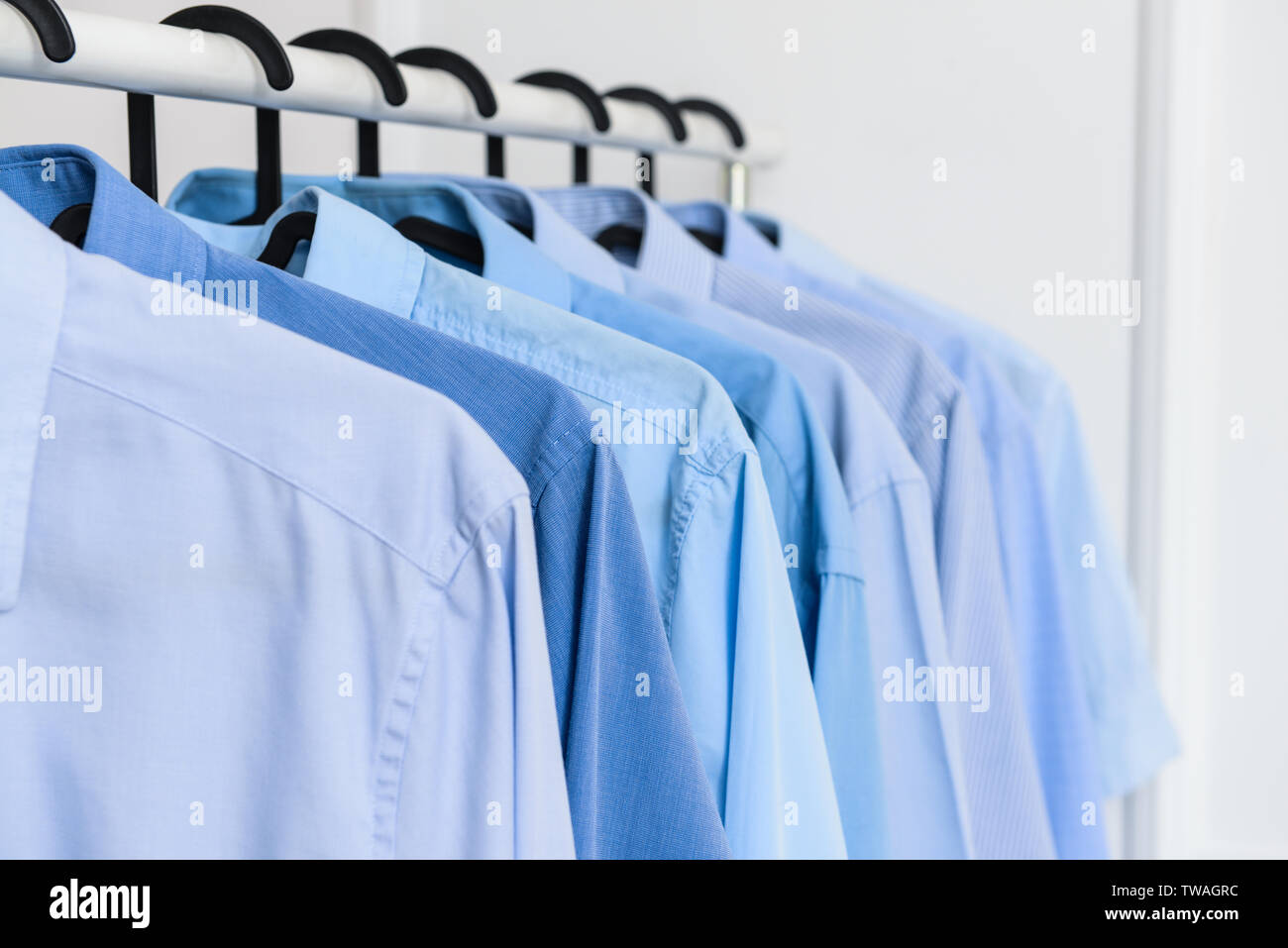 Rack with clothes after dry-cleaning near white wall, closeup Stock