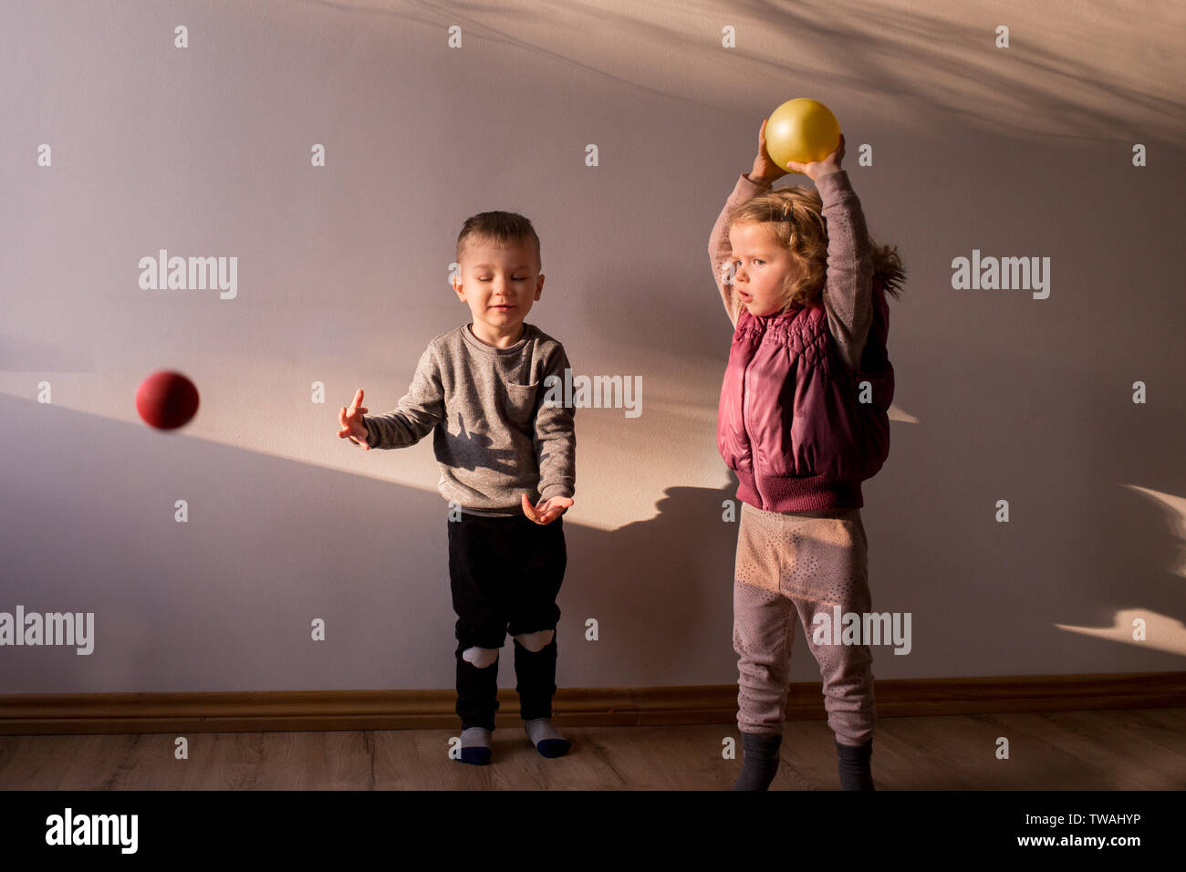 Two children playing inside, in a sunlit room, with little bouncing balls, throwing them up in the air Stock Photo