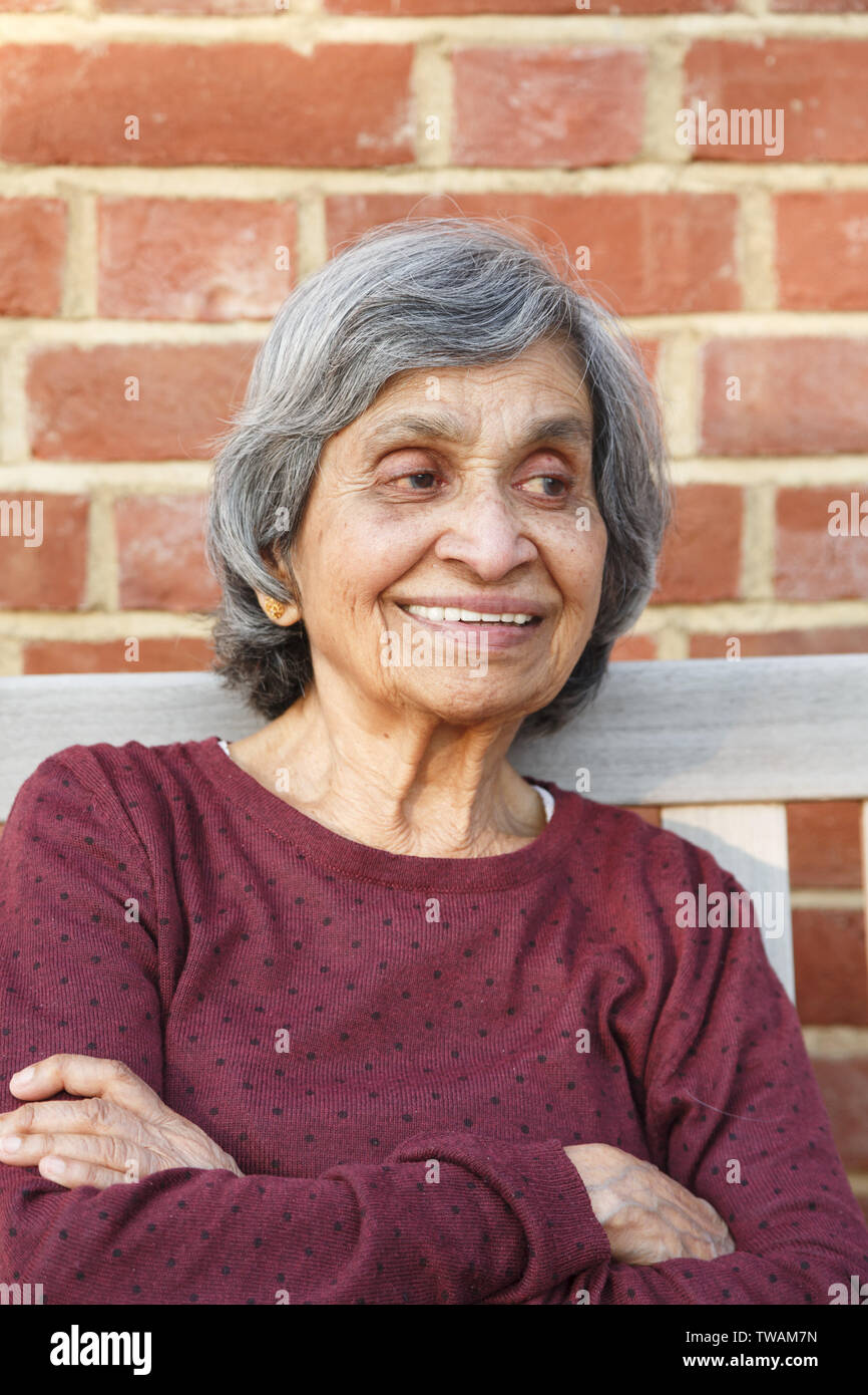 Old elderly Asian Indian woman sitting with a smiling face, depicting health and happiness in old age and retirement Stock Photo