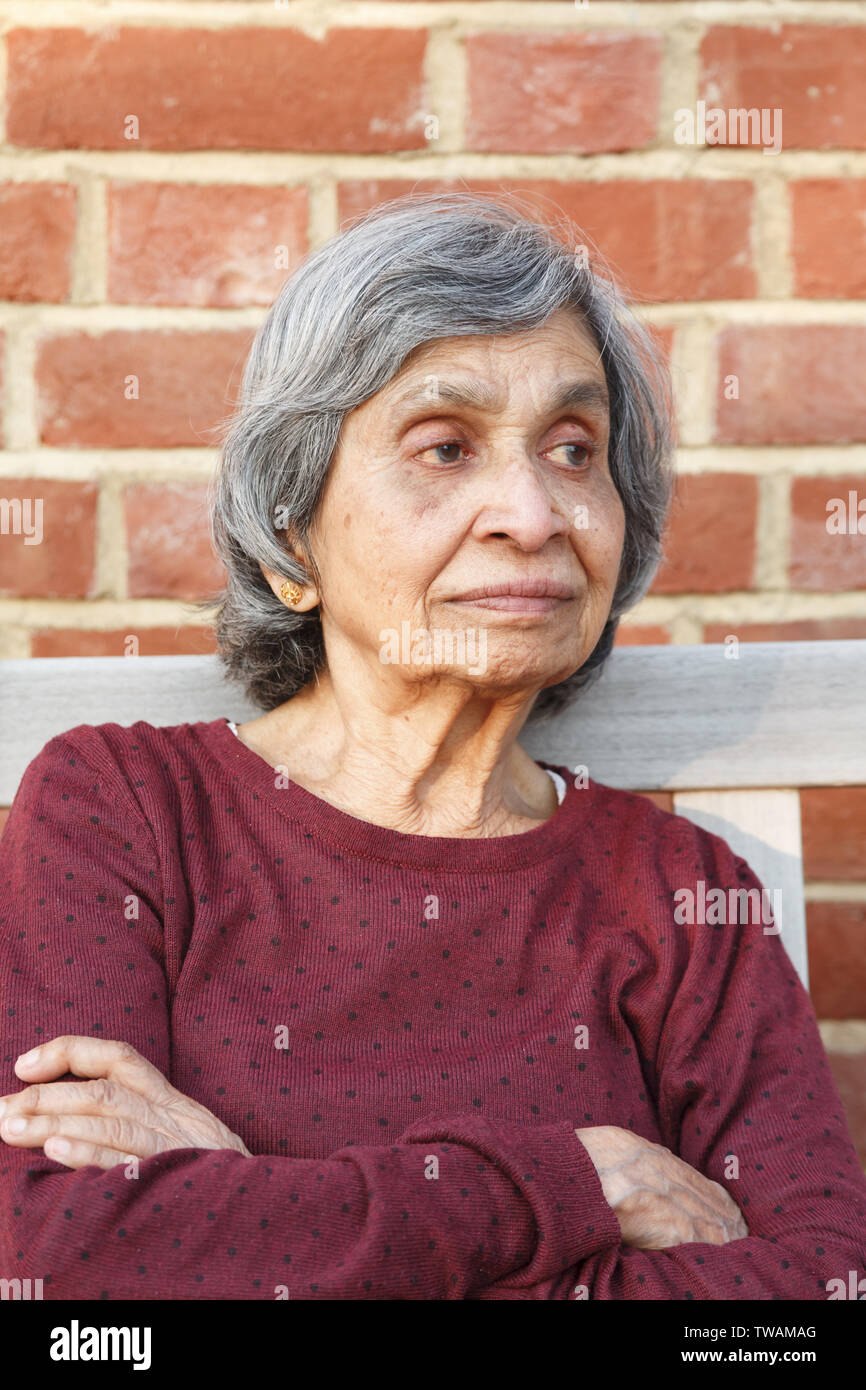 Elderly Asian Indian woman sitting alone. Healthy and slim appearance, may also depict loneliness or depression in old age. Stock Photo