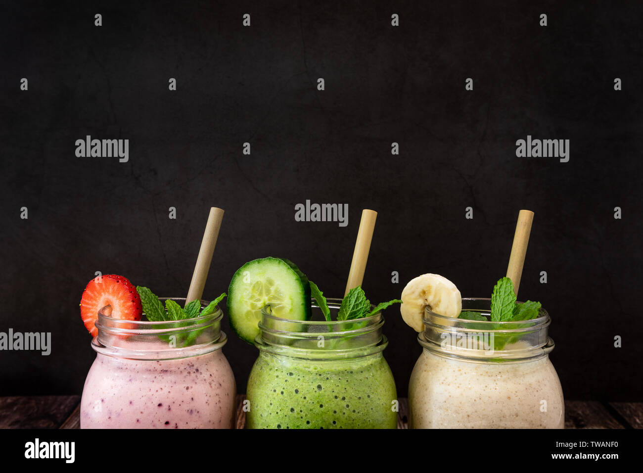 Delicious organic Banana, Strawberry and Cucumber, flax and chia seed fruit smoothies shot against a black slate background. Also pictured are eco Bam Stock Photo
