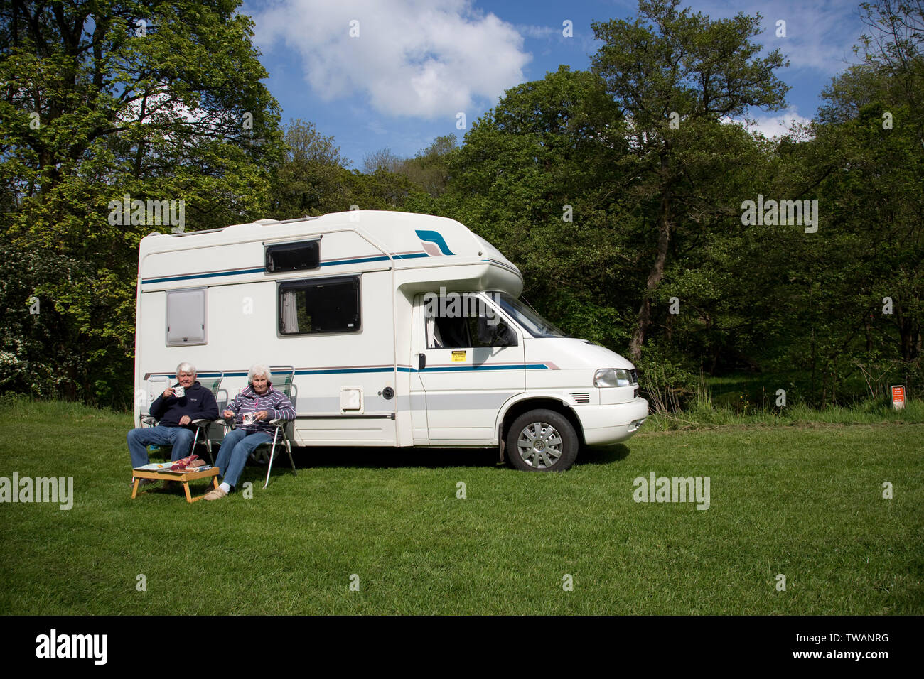 Elderly retired couple relaxing with cup of team in camping chairs outside motorhome in field, Peak District, Dervyshire, UK Stock Photo