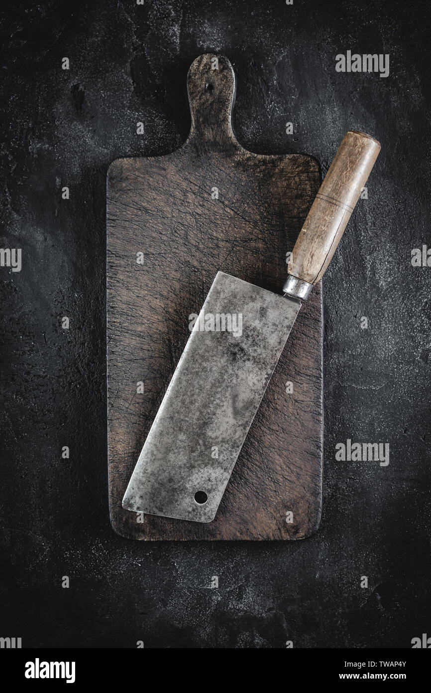 Old Butcher Meat Cleaver and Rustic Brown Wood Chopping Board on Dark Background Stock Photo