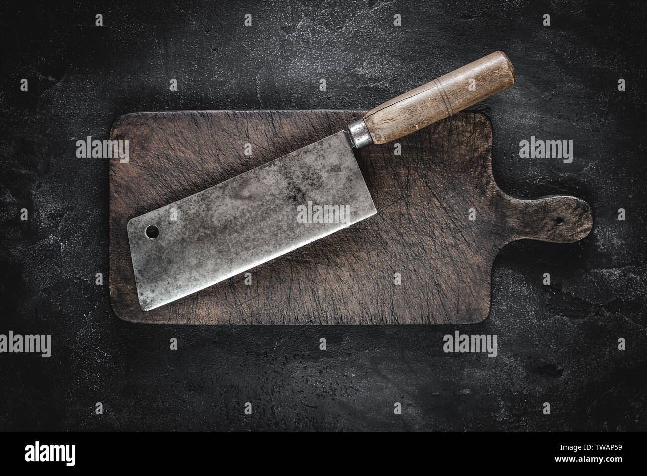 Old Butcher Meat Cleaver and Rustic Brown Wood Chopping Board on Dark