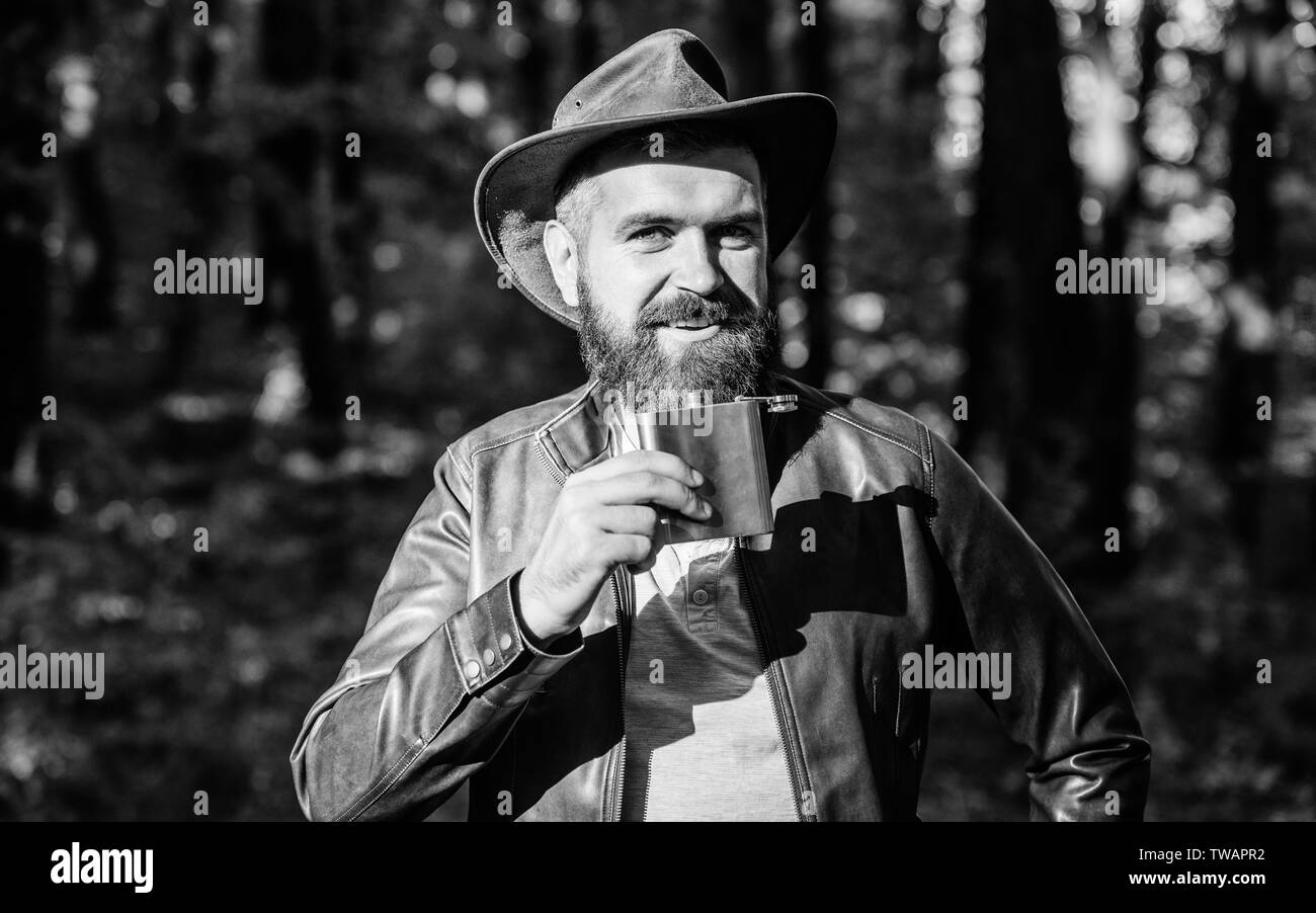 Country style. Bearded man in cowboy hat walk in park outdoor. man hipster relax in autumn forest. Spring weather. camping and hiking. mature male with brutal look drink alcohol from metallic flask. Stock Photo