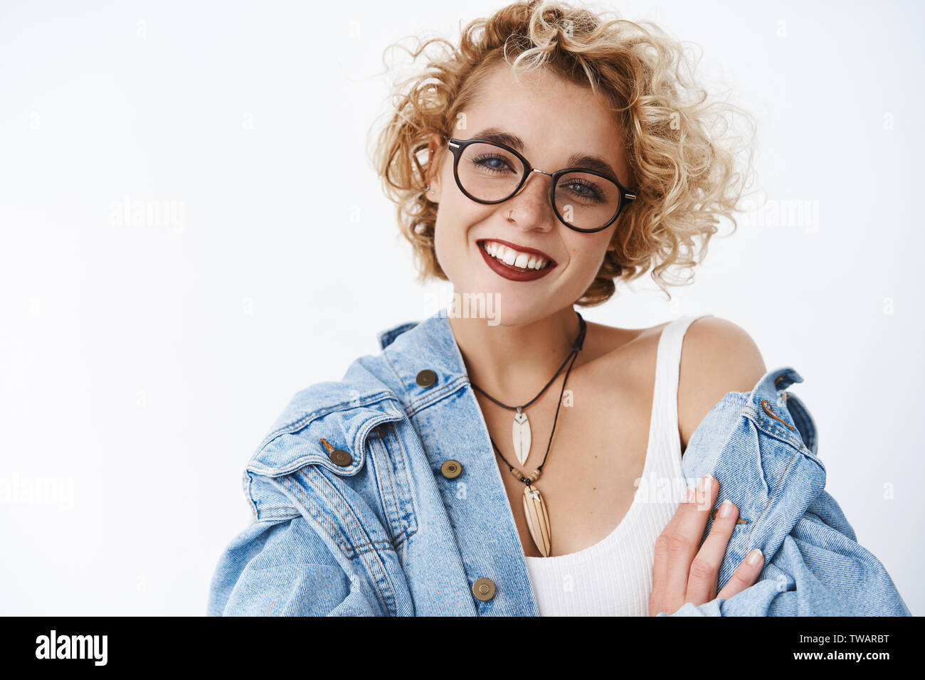 Happy delighted and attractive blond female with short curly hairstyle freckles and pierced nose wearing lipstick smiling joyfully tilting head Stock Photo