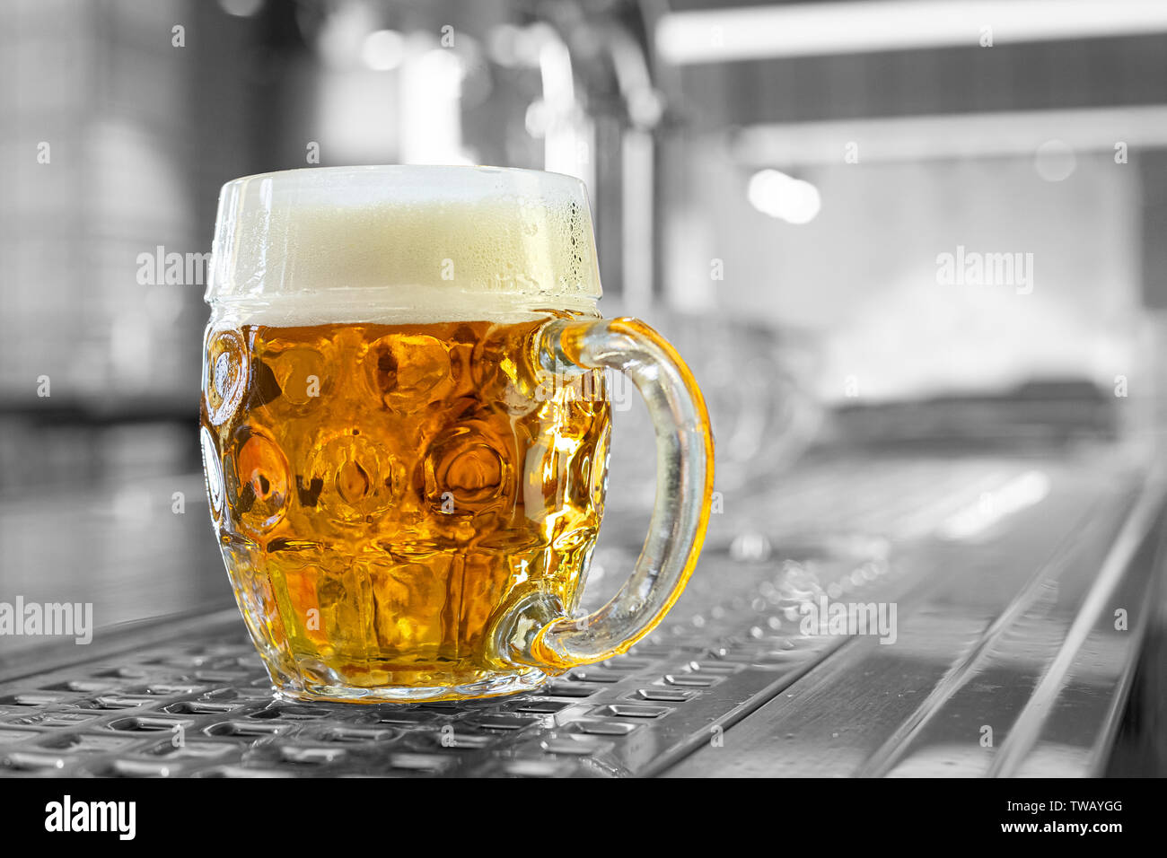 Freshly poured draft lager beer in a dimpled glass mug on stainless steel counter in a modern pub. Black and white background. Space for text. Stock Photo