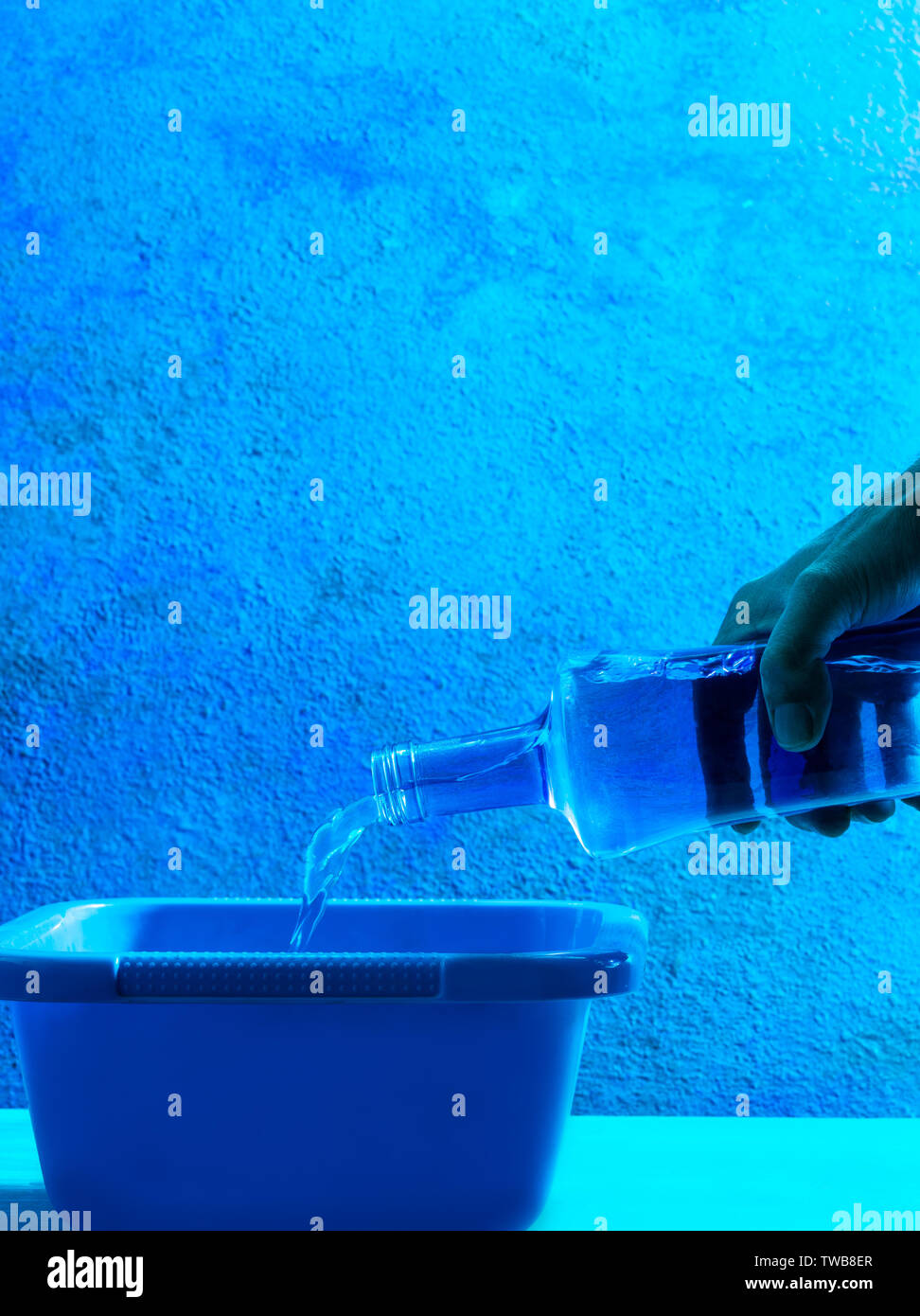 Blue glass bottle pouring water hand in all blue monochromatic bucket and wall Stock Photo