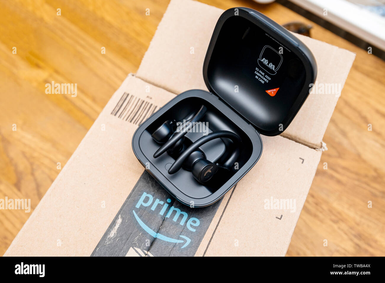 Paris, France - Jun 17, 2019: wooden table with Amazon Prime cardboard parcel and Powerbeats Pro Beats by Dr Dre wireless high-performance earphones waterproof and workout professional headphones Stock Photo