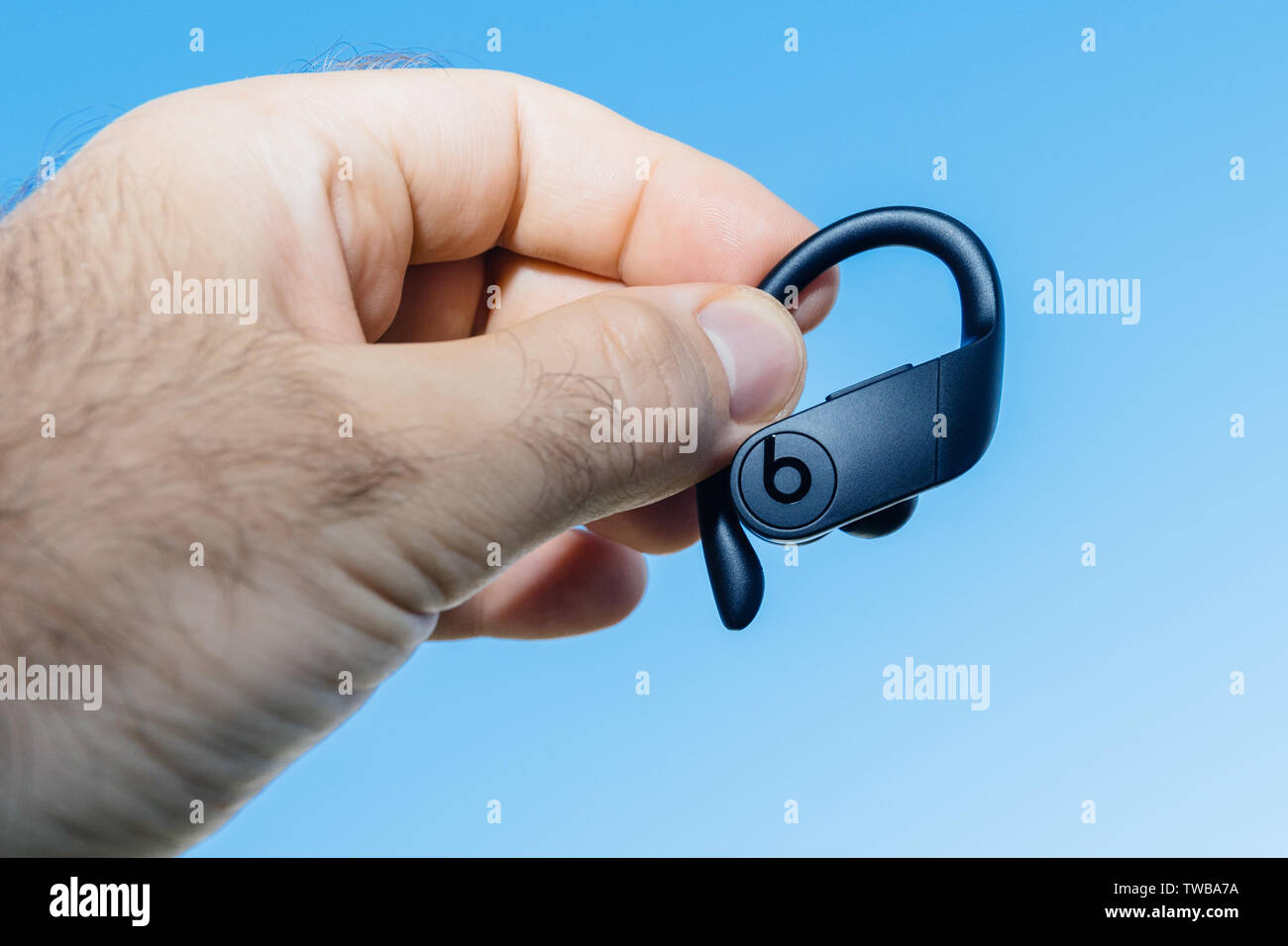 Paris, France - Jun 17, 2019: Close-up of man hand holding demonstrating new Apple Powerbeats Pro Beats by Dr Dre wireless high-performance earphone with integrated Siri - blue sky Stock Photo