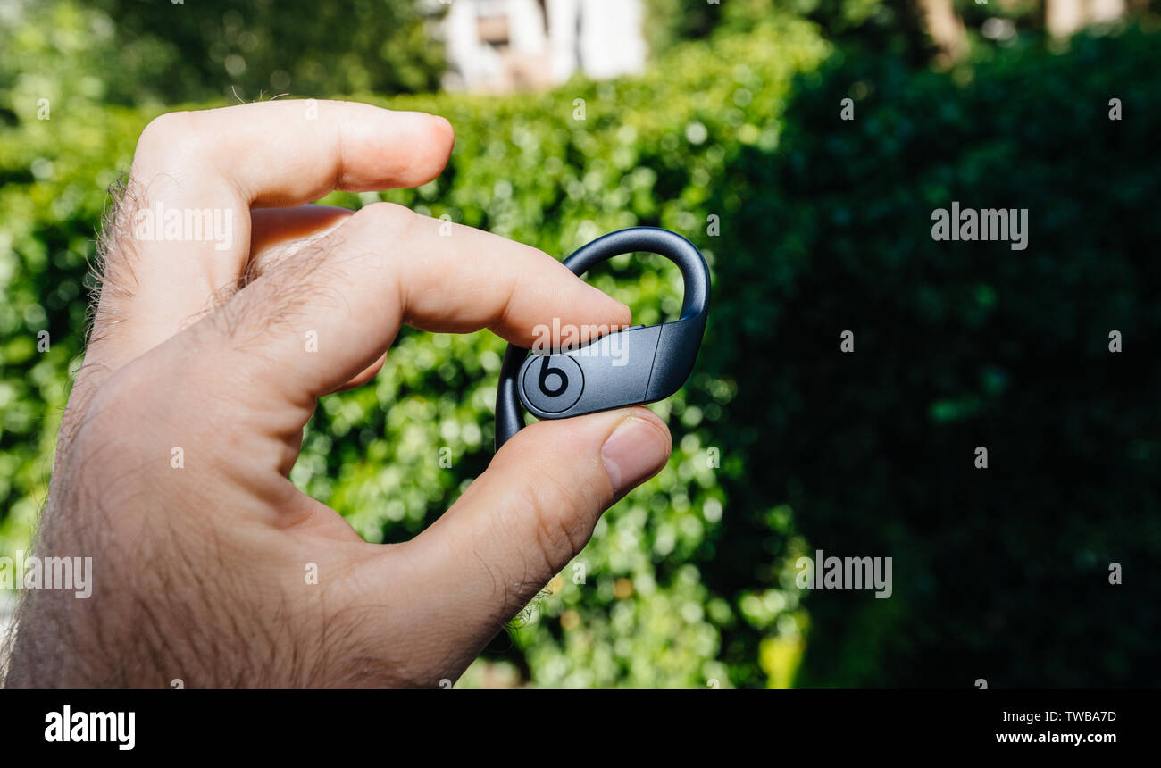 Paris, France - Jun 17, 2019: Close-up of man fingers holding new Powerbeats Pro Beats by Dr Dre wireless high-performance earphone with integrated Siri - green park forest background Stock Photo
