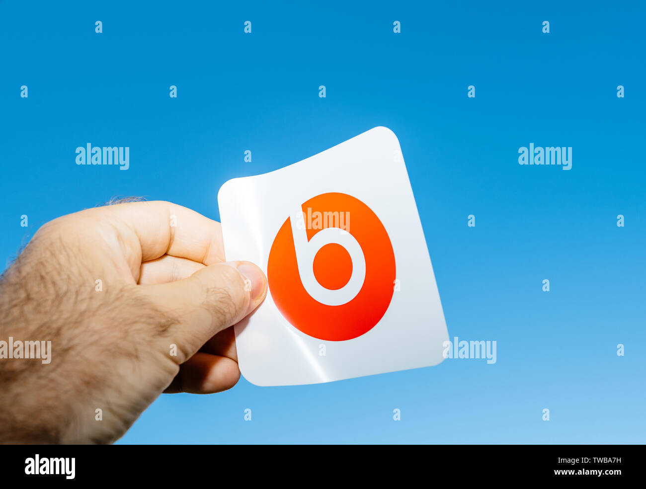 Paris, France - Jun 17, 2019: Man hand holding red sticker with logotype insignia brand during Powerbeats Pro Beats by Dr Dre unboxing - blue clear sky in the background Stock Photo